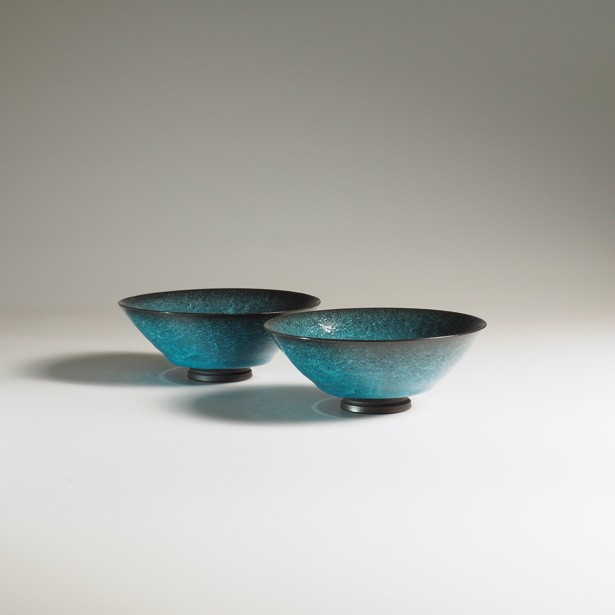 Two jade green japanese ceramic bowls on a light gray background