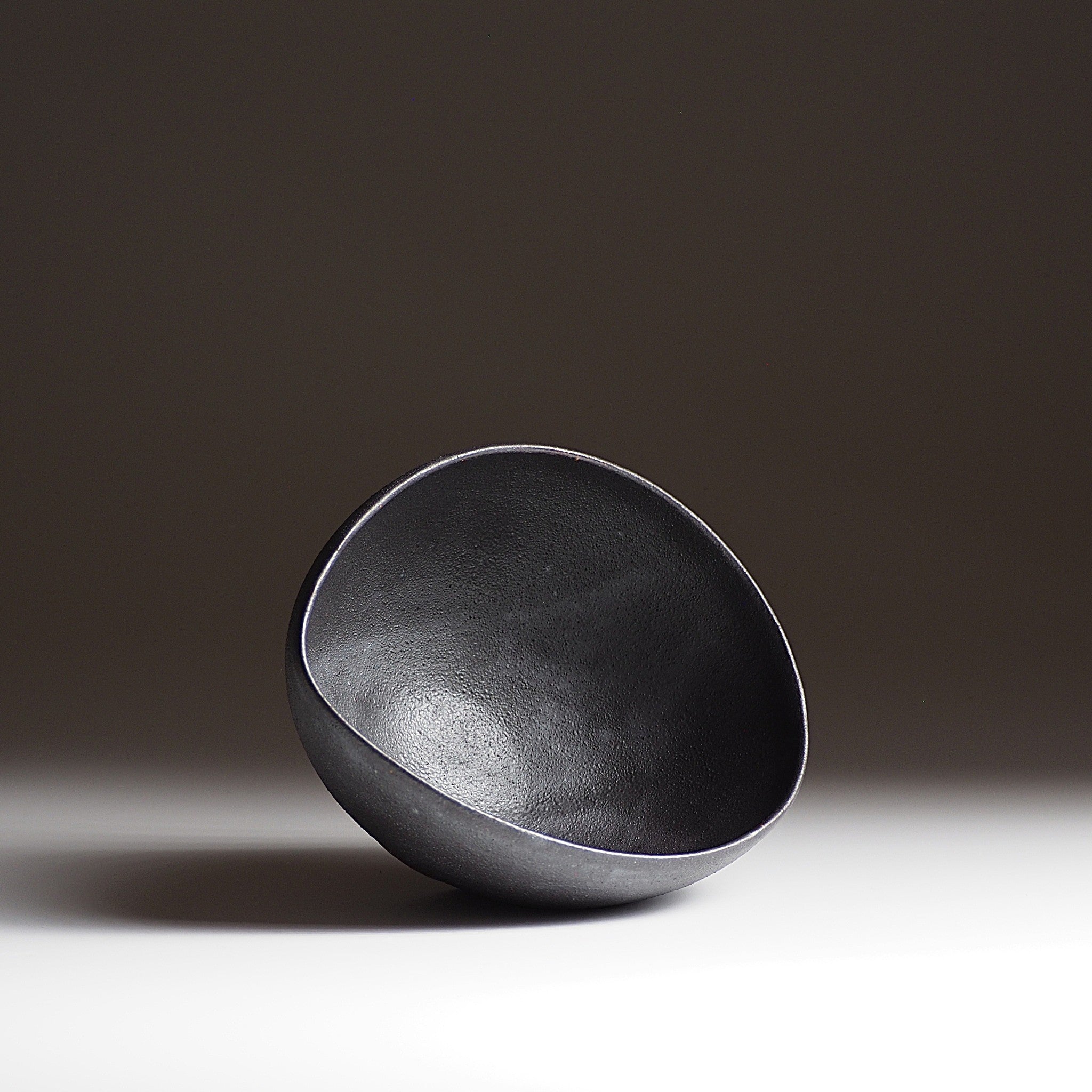 Handcrafted black Japanese ceramic bowl on a dark gradation background, Tsukushi