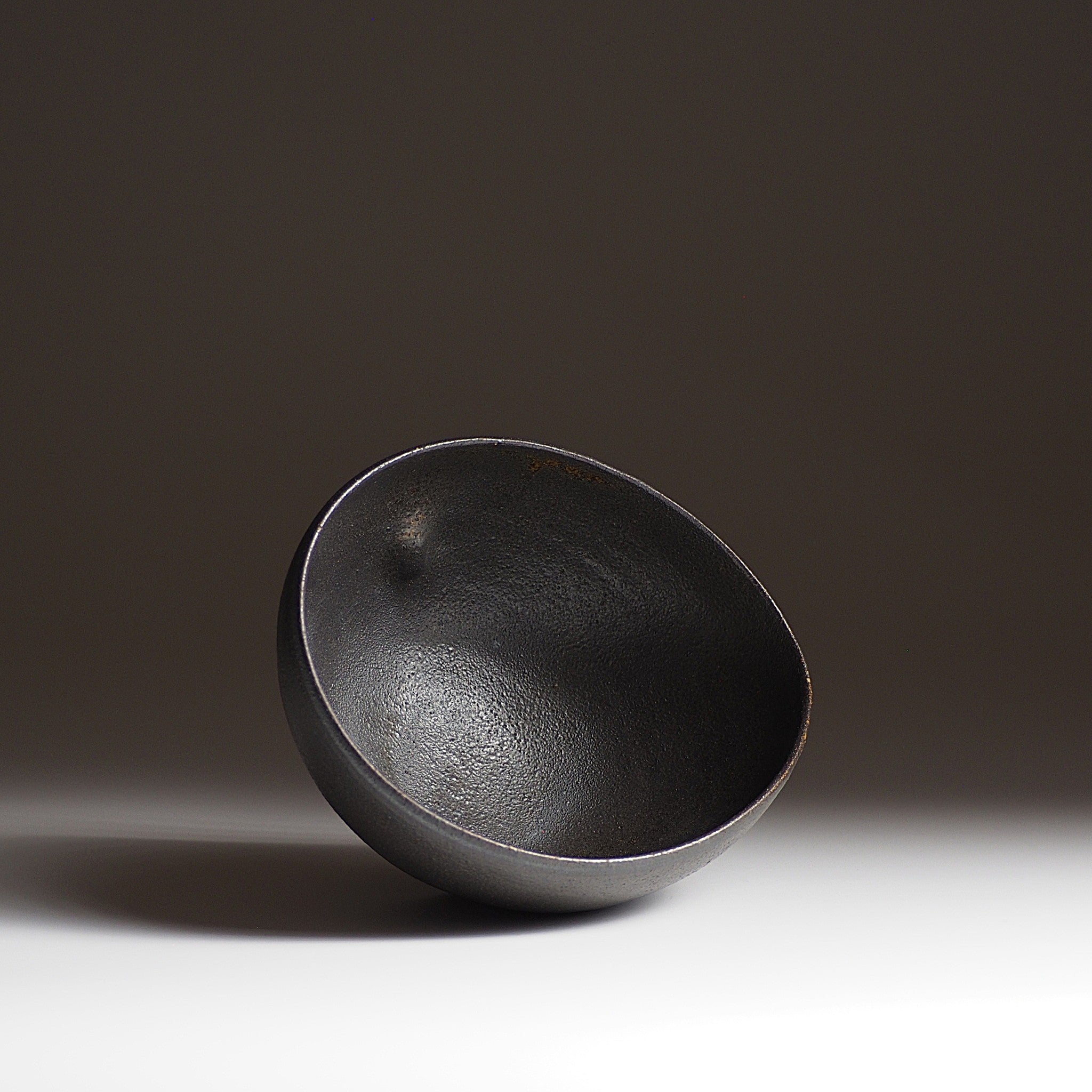 Top view of handcrafted black Japanese ceramic bowl on a dark gradation background, Tsukushi