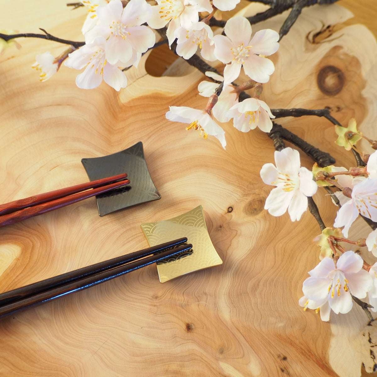 Two Japanese Chopsticks and two chopstick rests on a wooden surface with cherry blossoms. Tsukushi