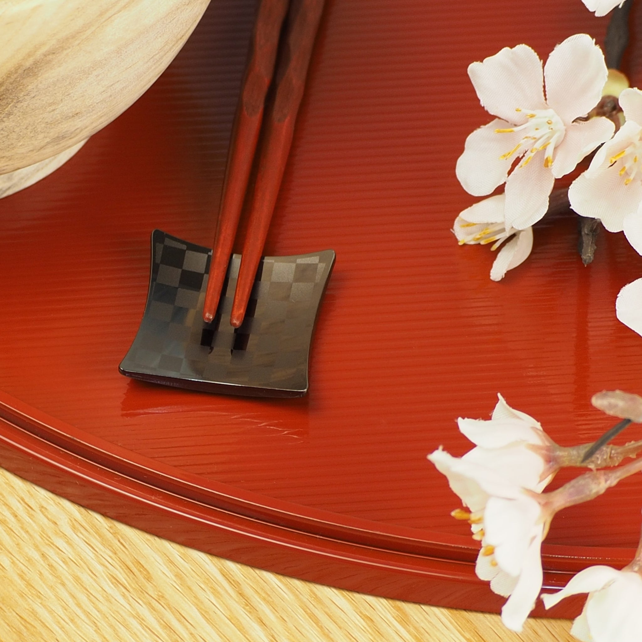 Chopsticks resting on a Japanese black chopstick rest on a red tray. Tsukushi