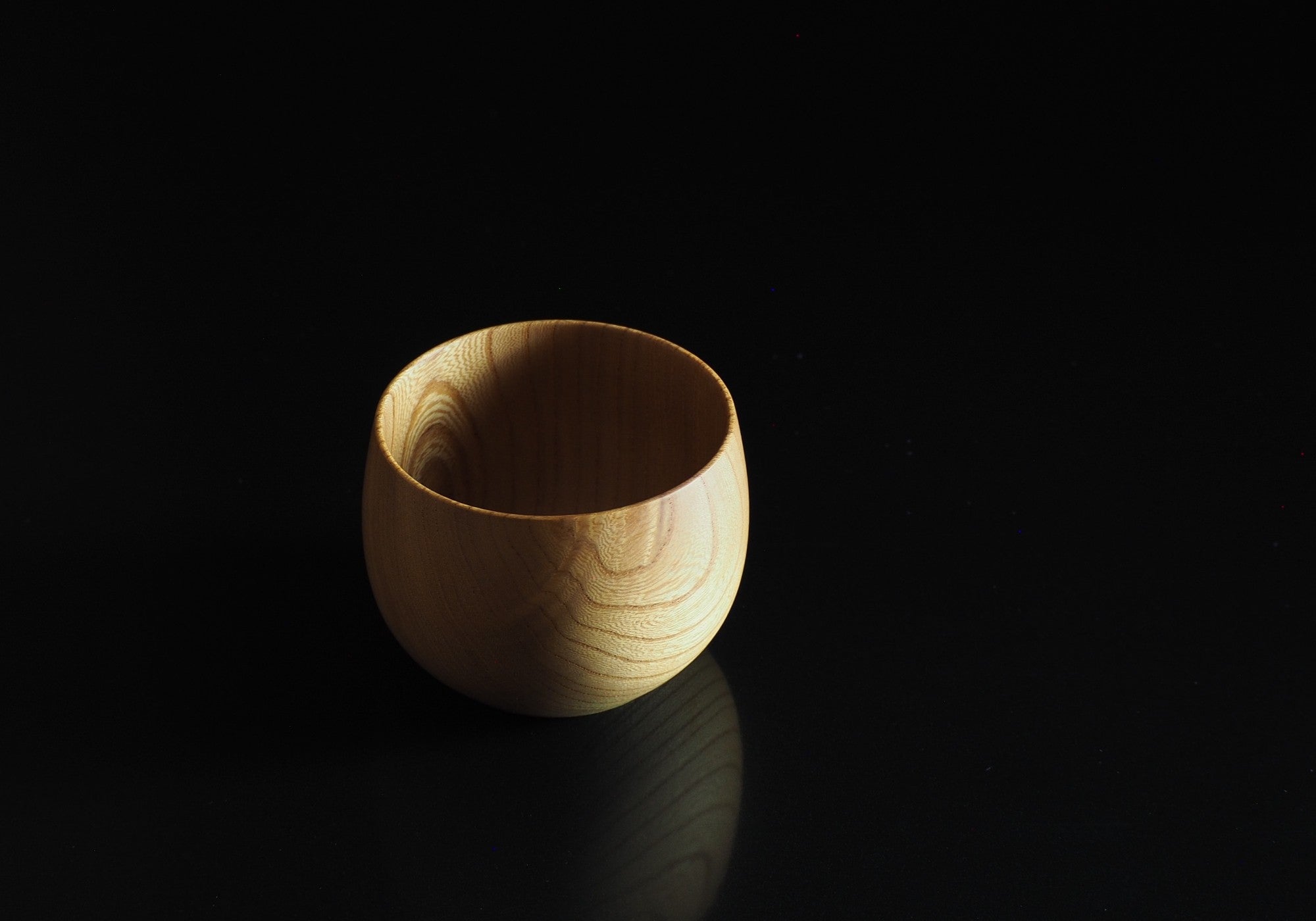 A Japanese wooden cup on a black reflective surface. Tsukushi