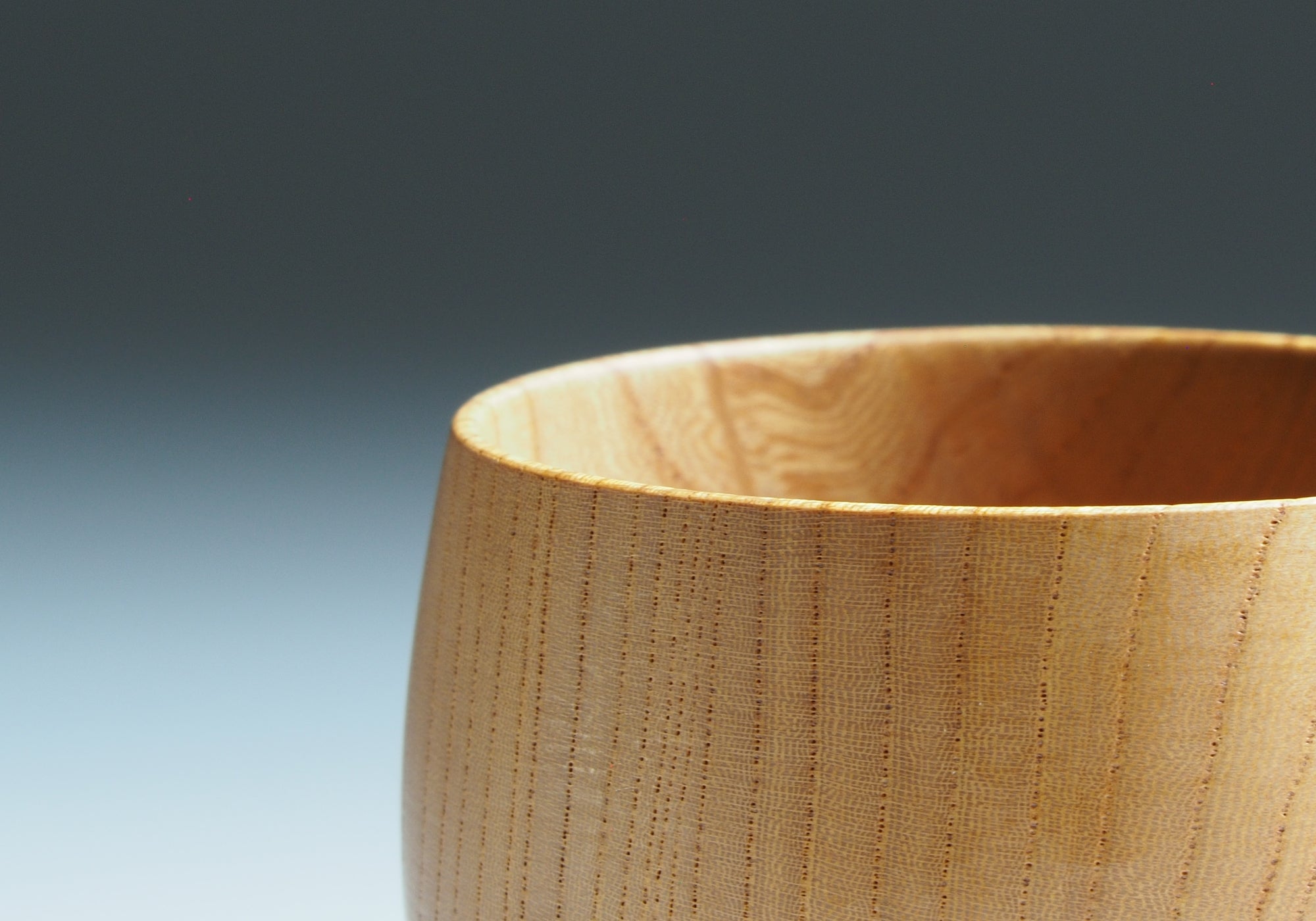 A close-up of a wood yunomi cup with a gray background. Tsukushi