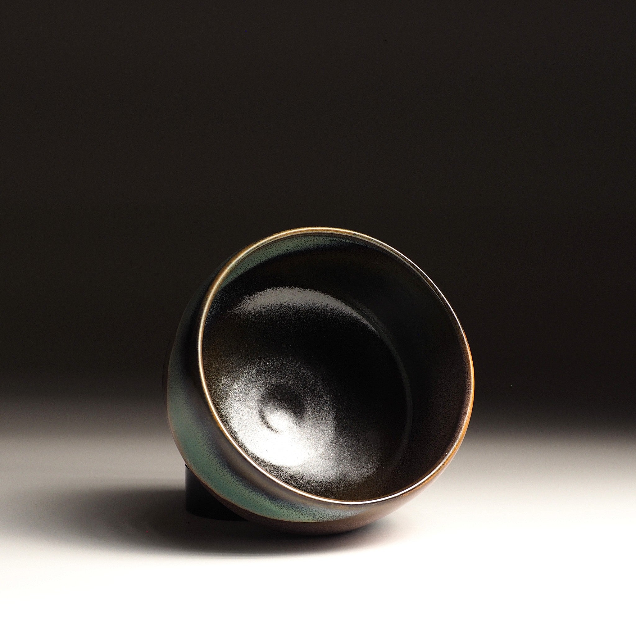 A top view of Japanese ceramic matcha bowl adorned with an aurora against a black background. Tsukushi