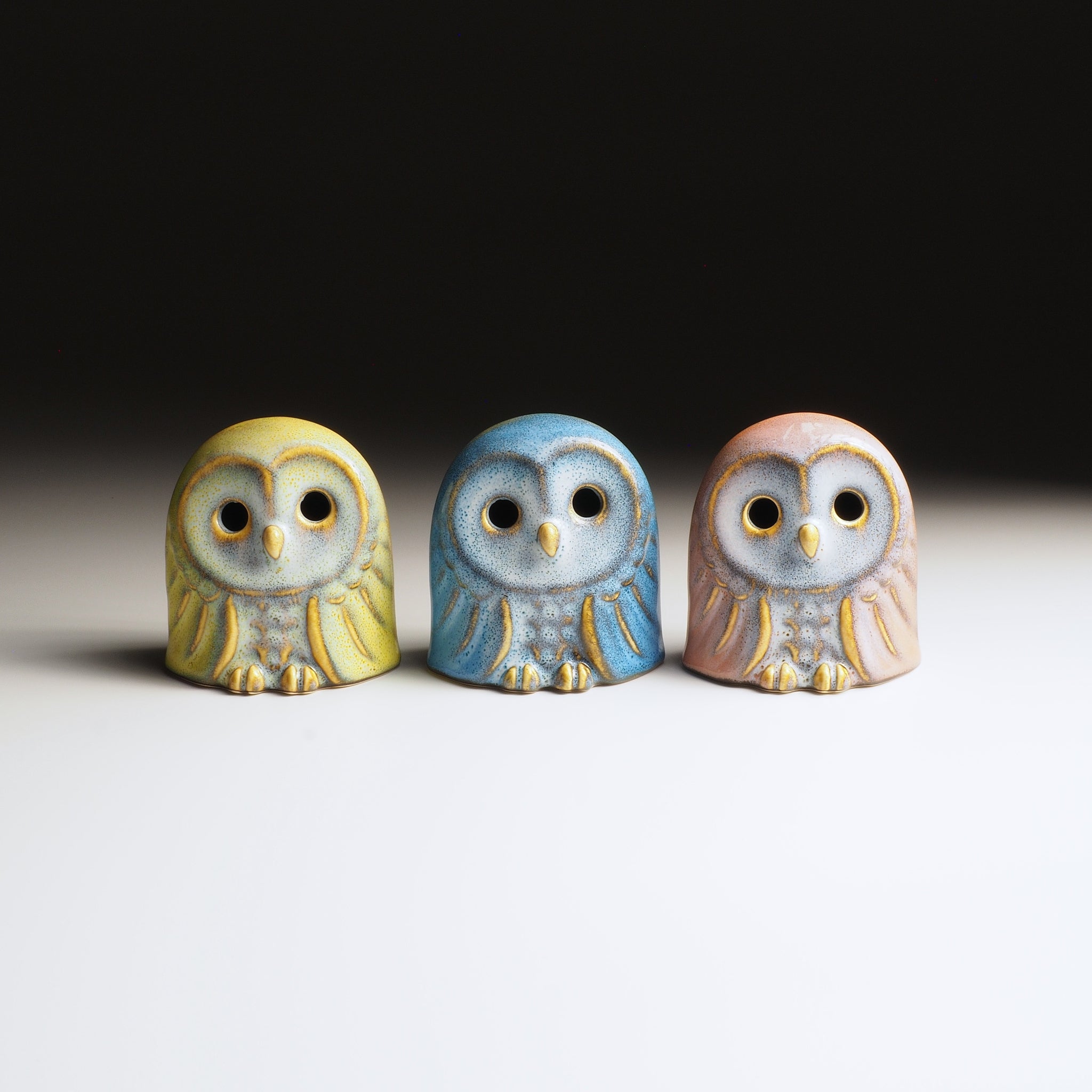 Three Japanese ceramic owl figurines in different colors on a neutral background