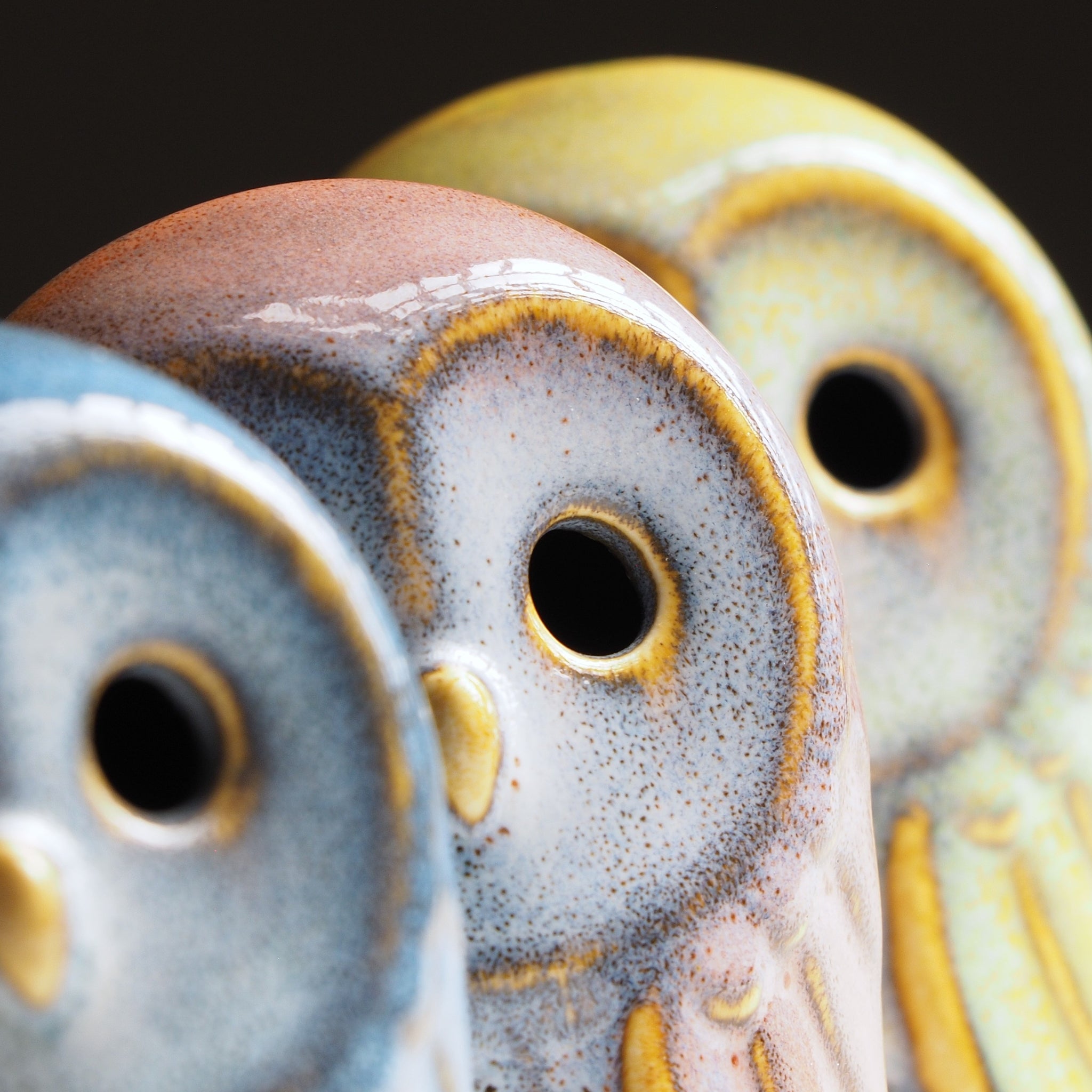 Close-up of ceramic owl figurines with textured glaze on a dark background