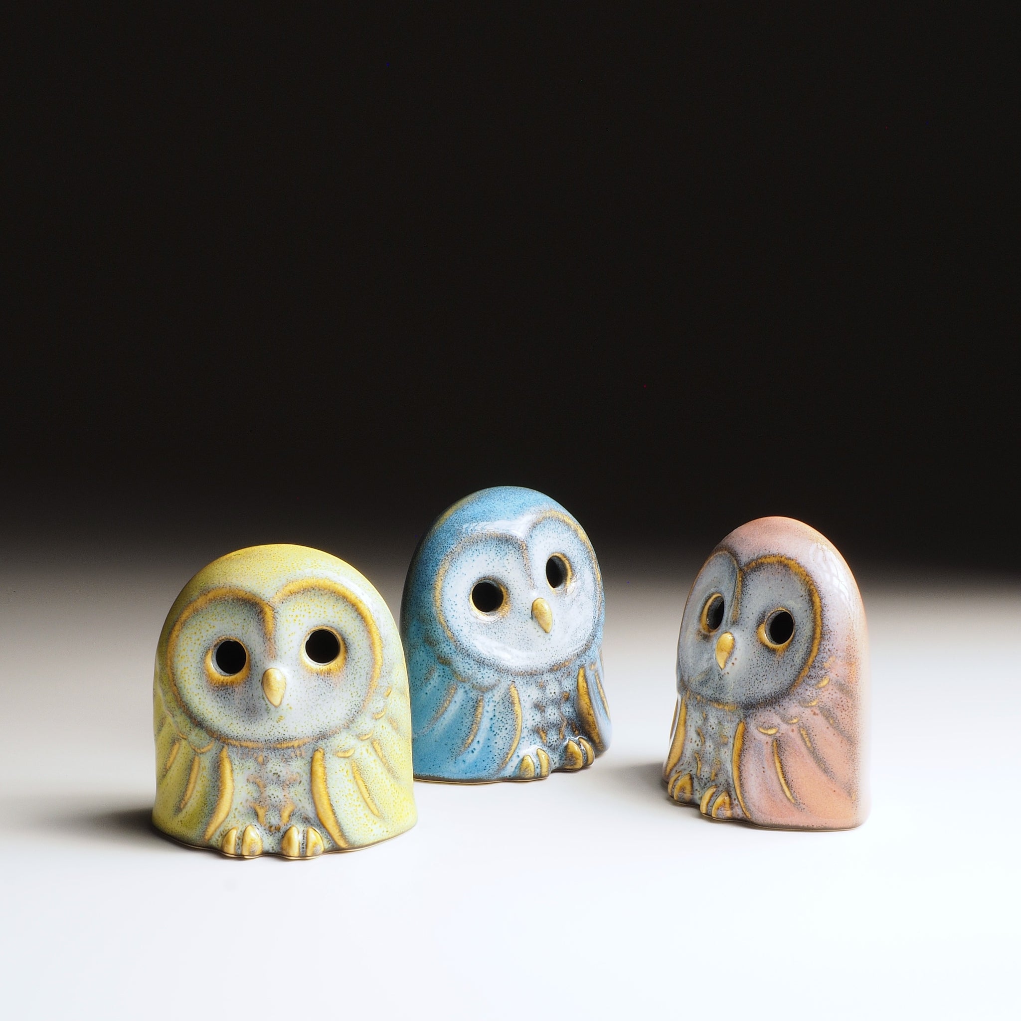 Set of three Engifuku owl figurines by Kazuhiro Kojima in yellow, blue, and pink speckled glazes, hollow eyes, front view.
