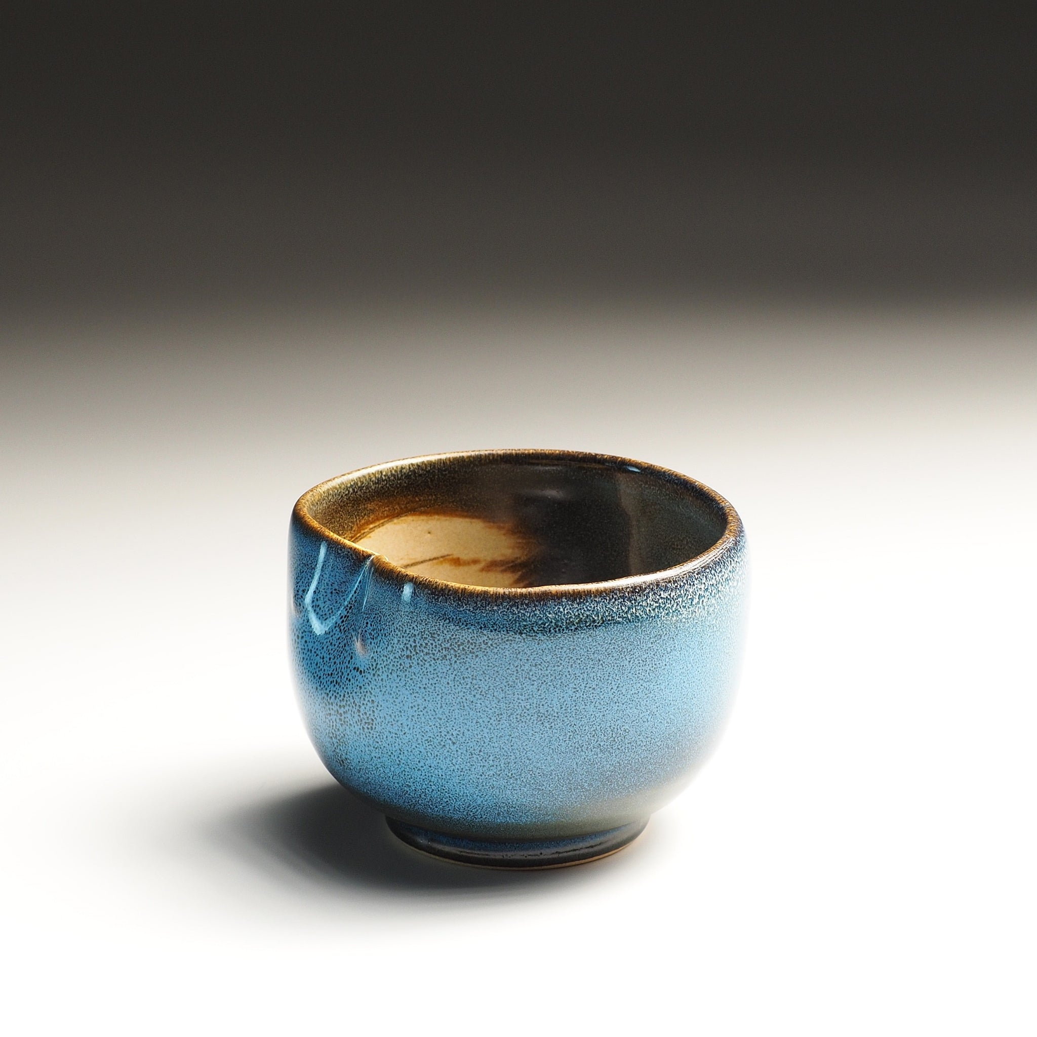 Blue ceramic teacup with a dark interior on a gradient background