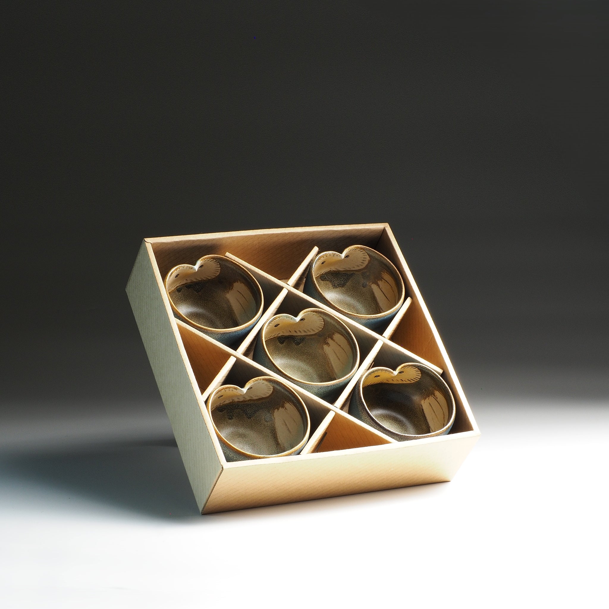 Set of five Japanese pottery teacups in a gift box on a gradient background.