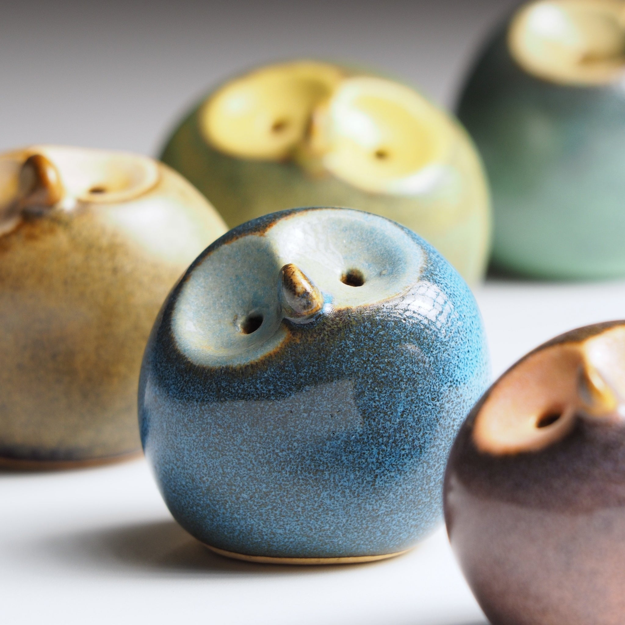 Close detail of Gofuku ceramic owl figurines showing varied glaze textures, gold facial features, and handcrafted surface variations.