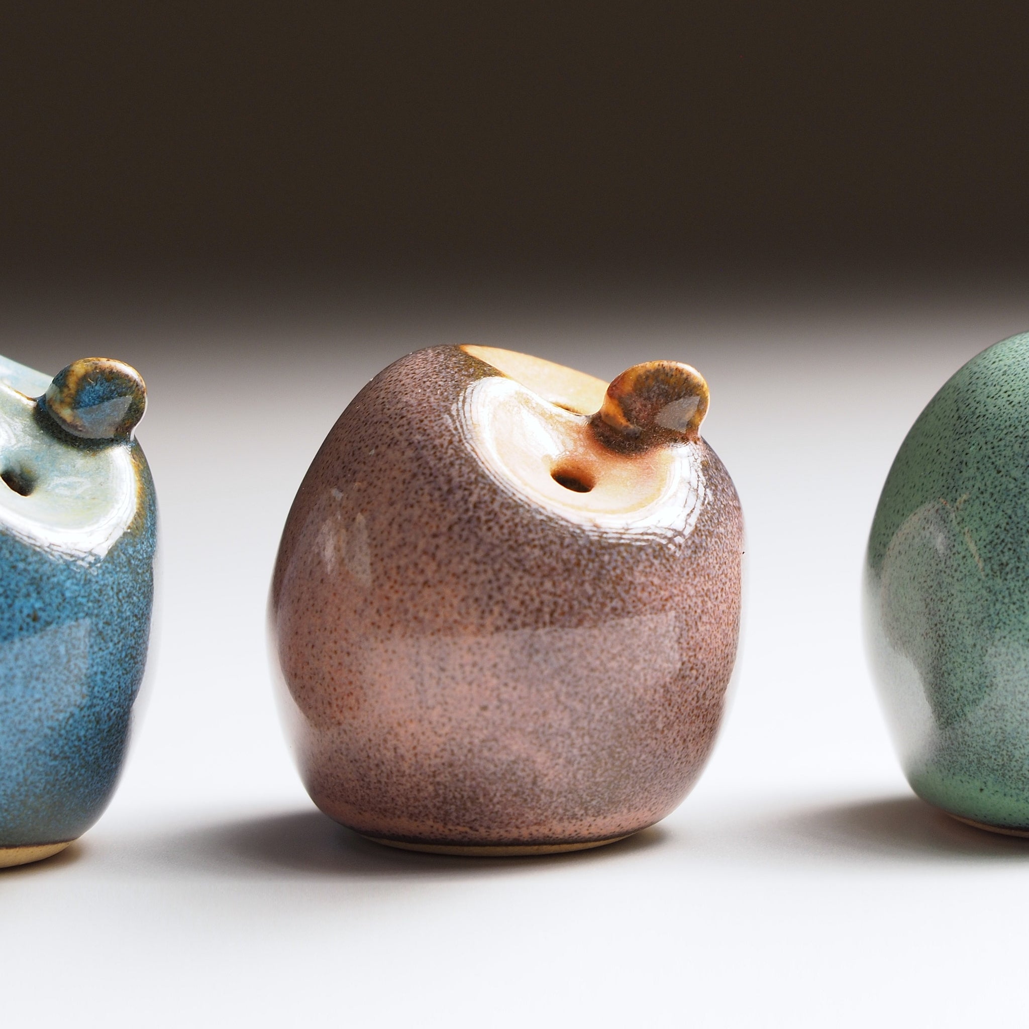 Three ceramic owls figurines with textured finishes on a neutral background