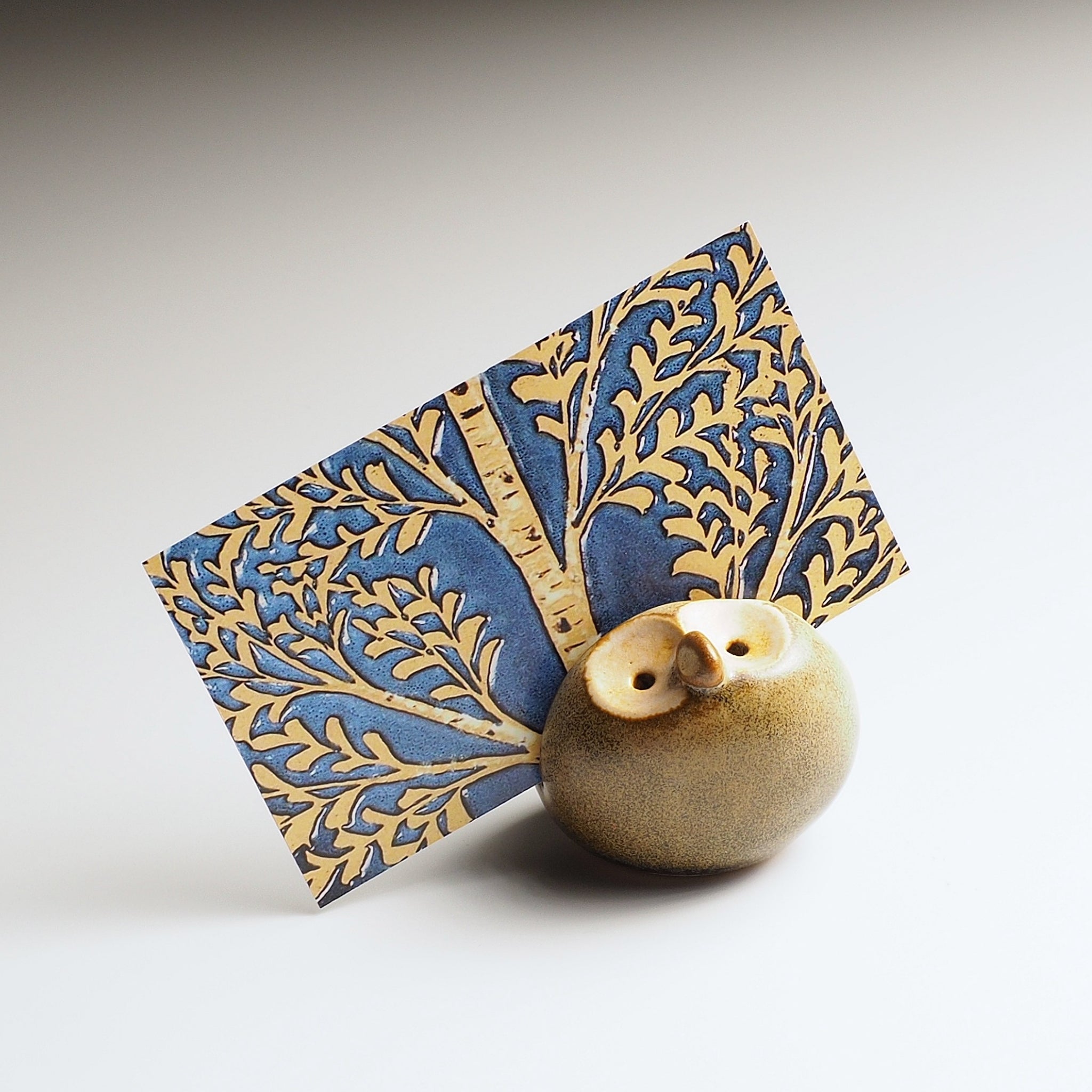 Warm sandstone Gofuku ceramic owl figurine with decorative blue and gold leaf-patterned backdrop. Handcrafted Japanese pottery.