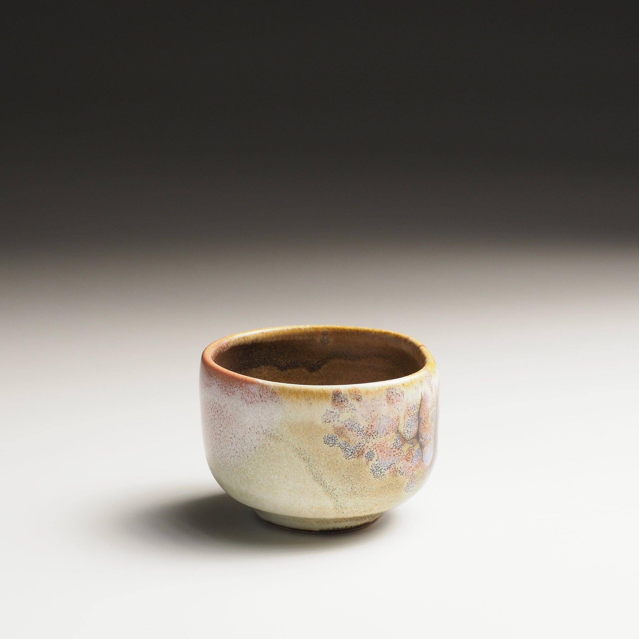 Fornt view of a Japanese guinomi with sakura decorations on a gradient background