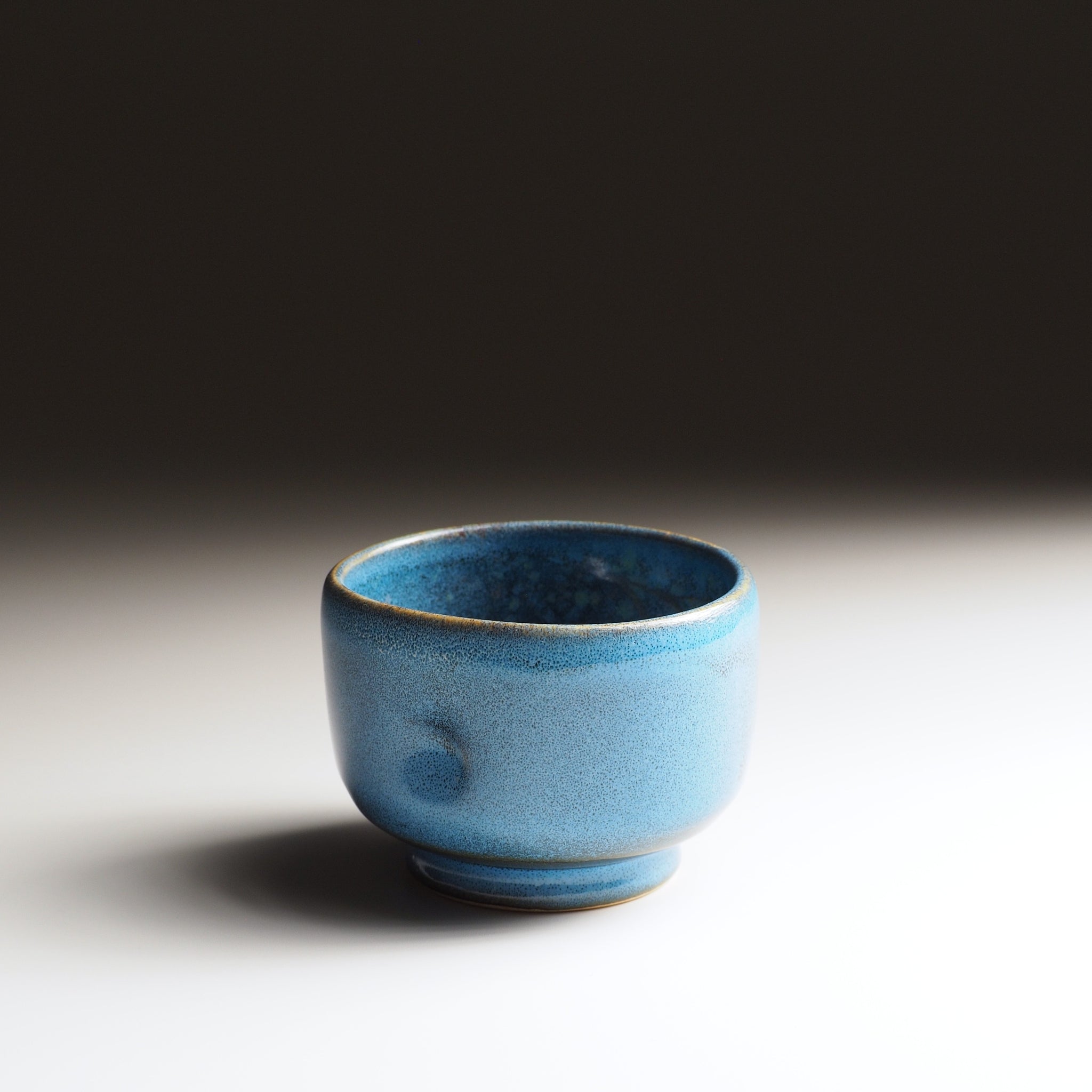 Side view of the Maru Komorebi Yunomi blue teacup on a faded background.