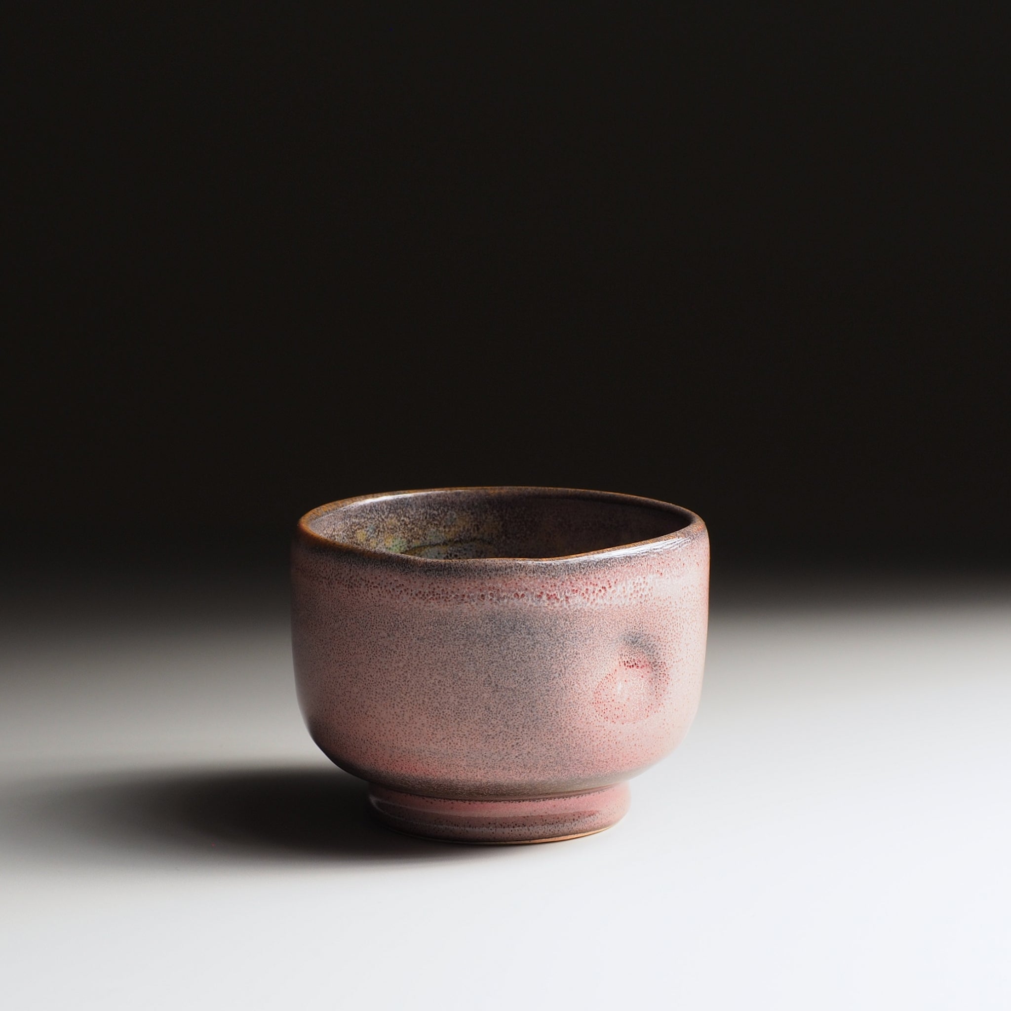 Ceramic Japanese teacup with a dark pink glaze on a light gray background