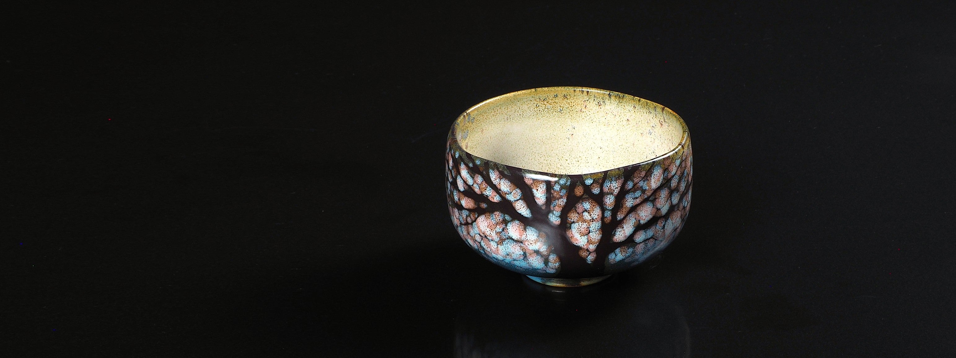 Handcrafted matcha bowl with tree pattern on a black background. Tsukushi