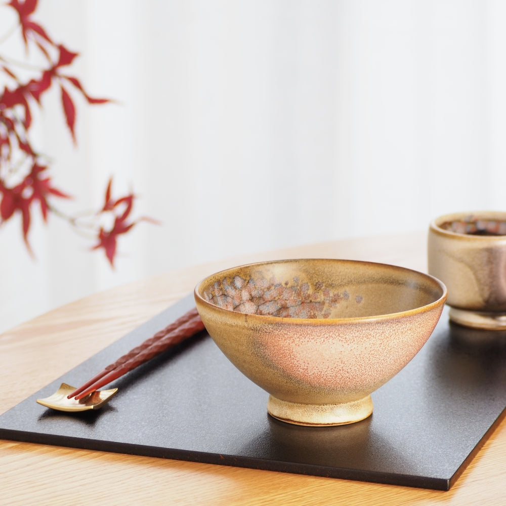 A Japanese ceramic rice bowl and a teacup on a black tray with red leaf in the background. Tsukushi