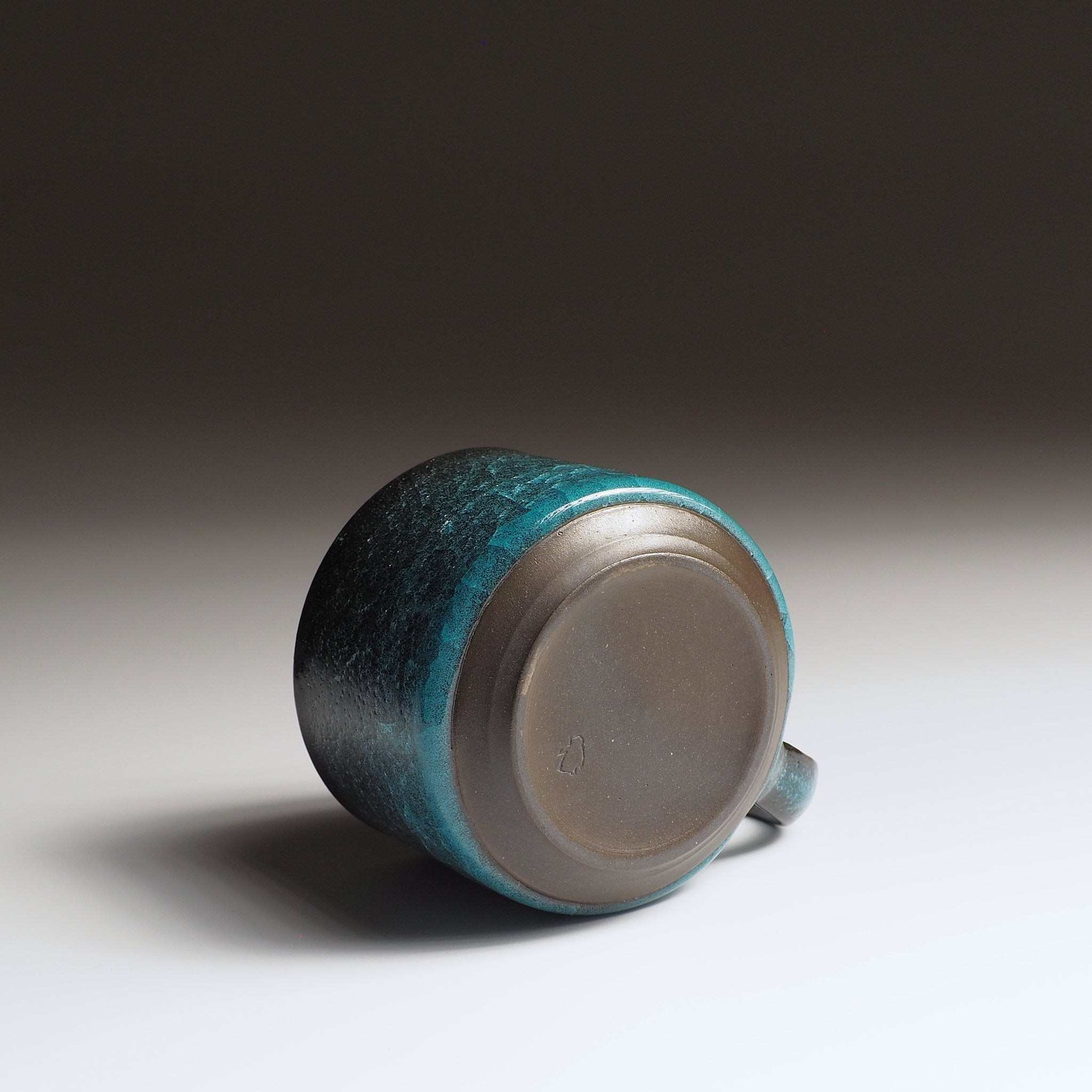 Unglazed base of handcrafted Japanese pottery coffee cup showing raw clay foot, emerald green kannyū glaze visible at rim, Usurai Pottery Kyoto