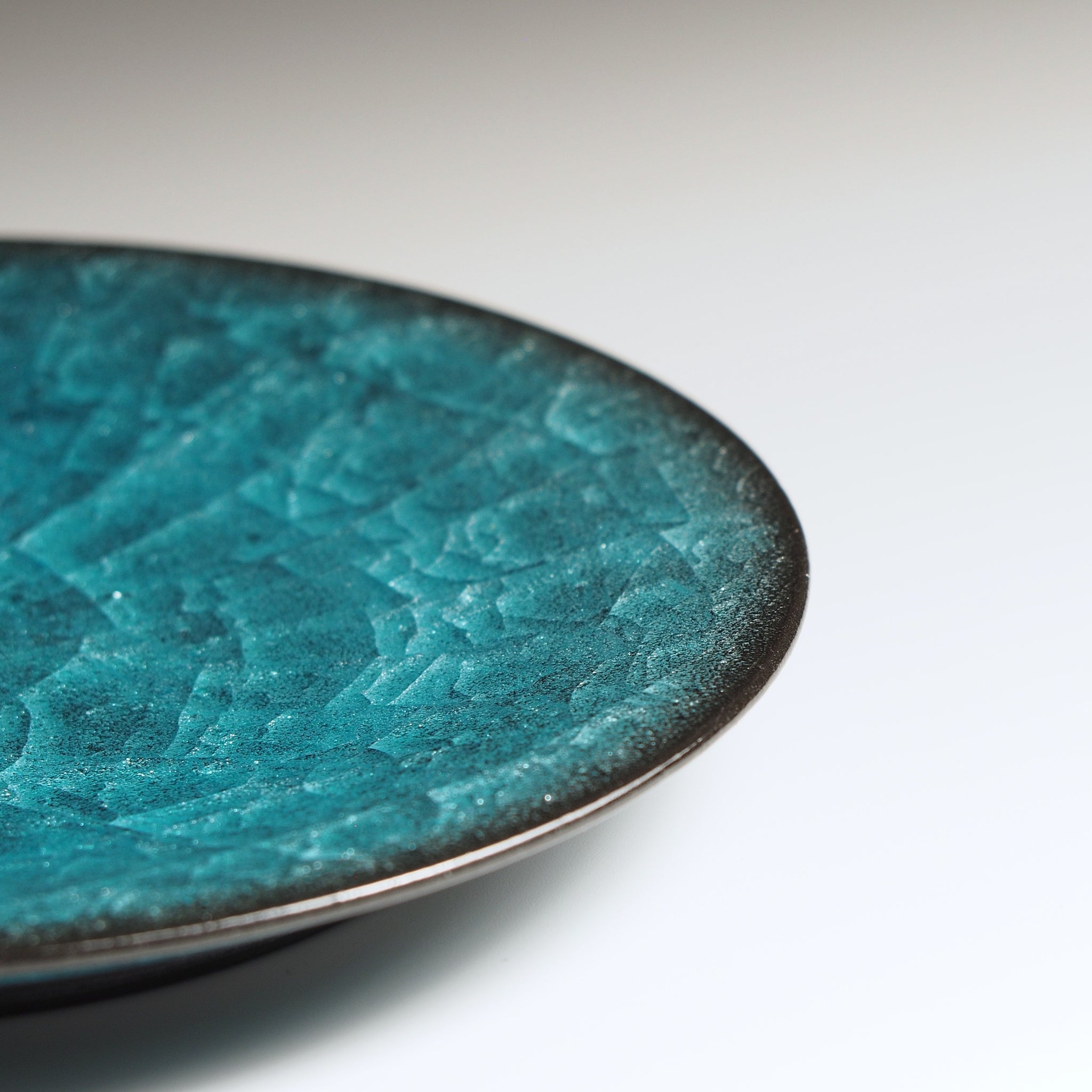 Close-up of teh Seika Japanese pottery saucer showing kannyū ceramic crazing glaze texture, emerald green, on a faded background