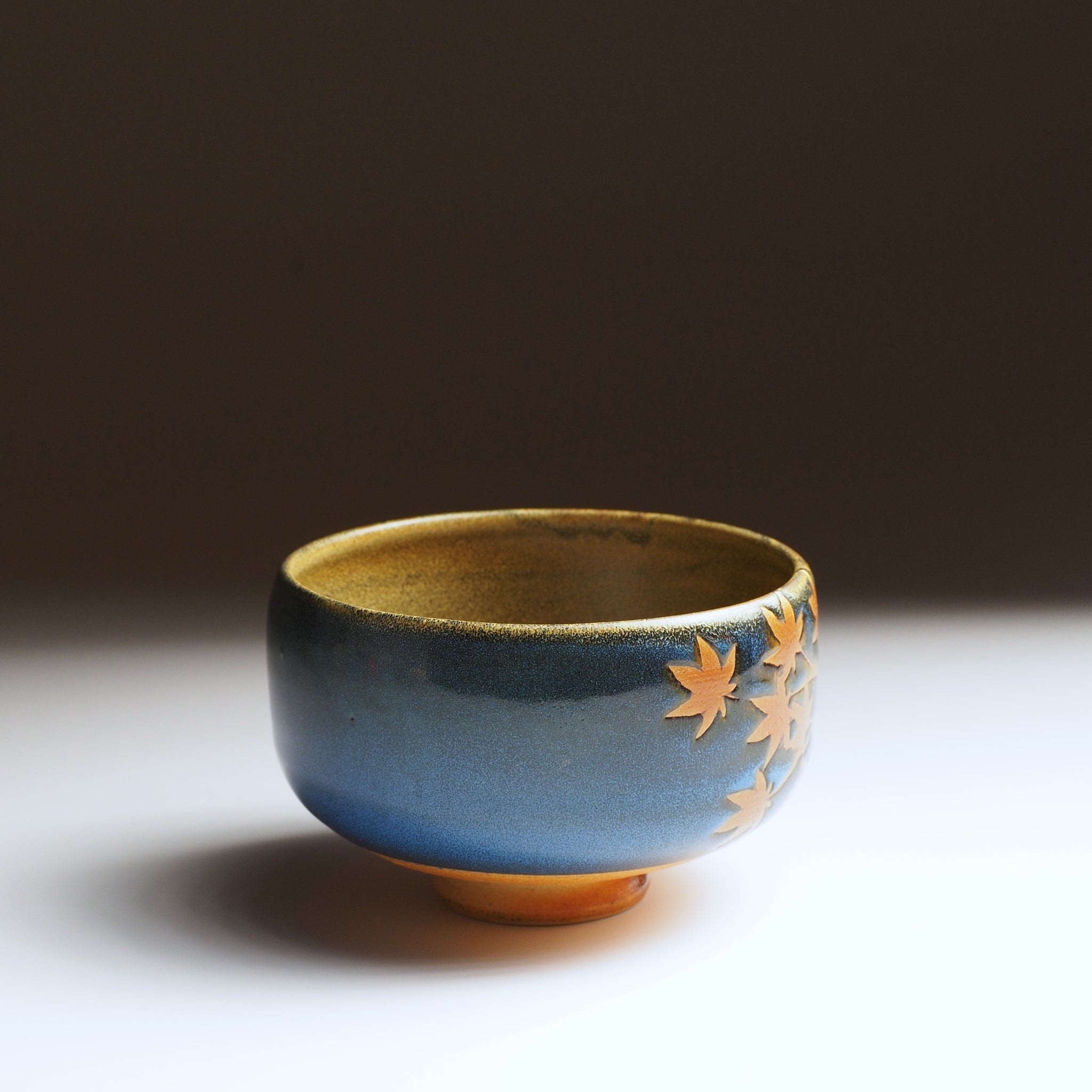 Sōshū matcha bowl, three-quarter view, momiji leaves in amber clay, open rim and blue glaze visible