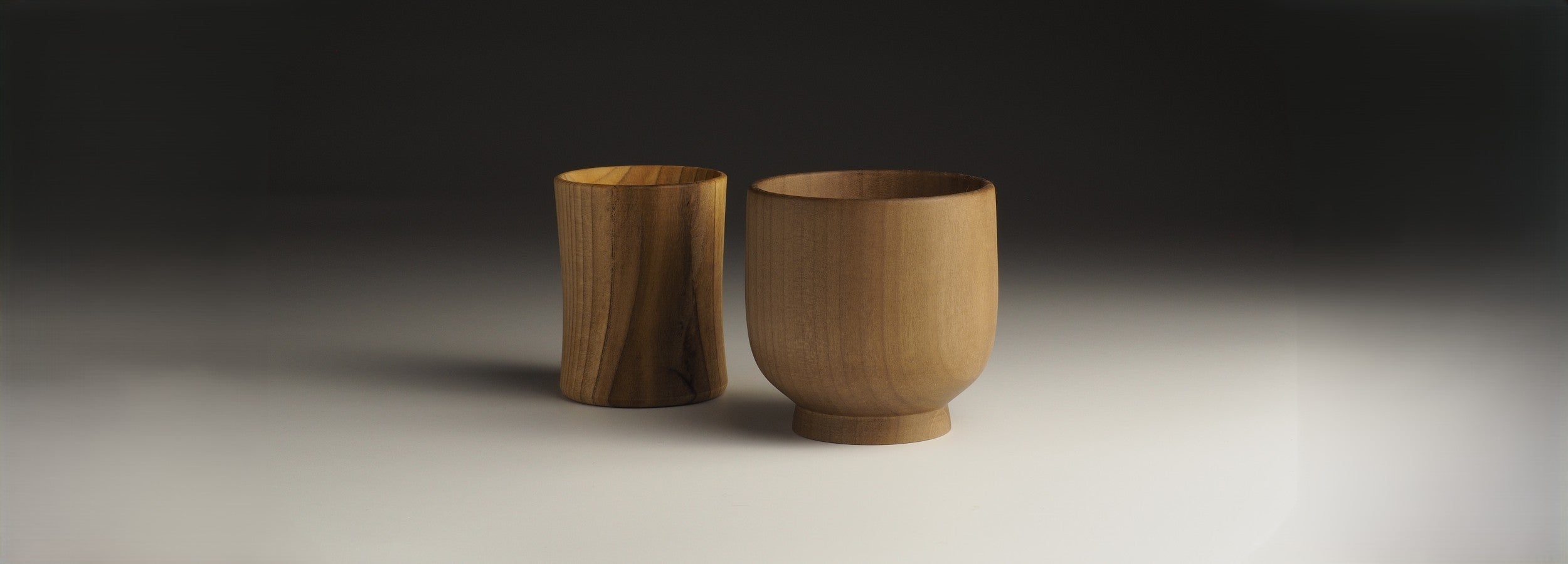 A wooden Japanese Sake Cup and a wooden Japanese tea mug on a gray background. Tsukushi