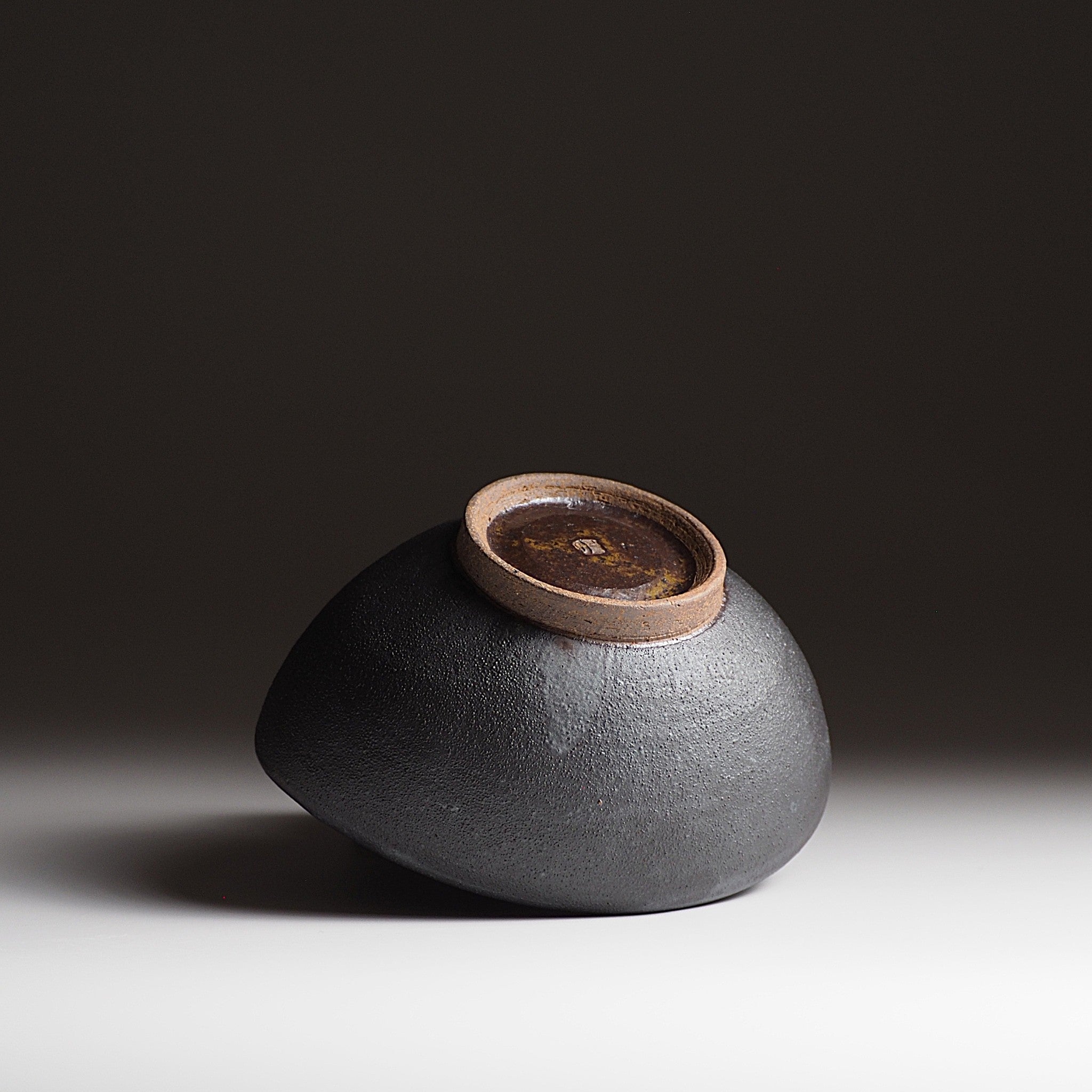 Handcrafted  black Japanese ceramic bowl with a brown bottom on a dark gradation background, Tsukushi