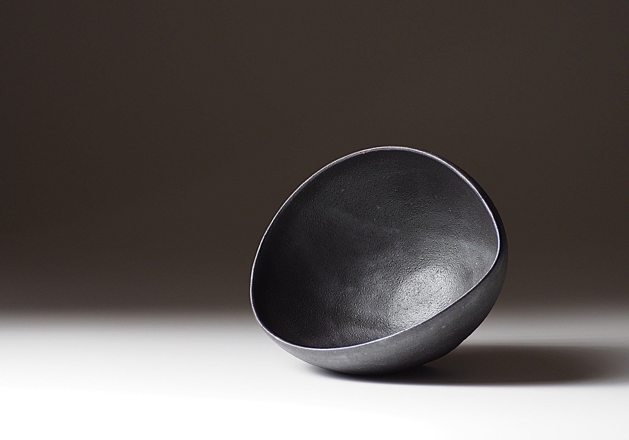 A handcrafted Japanese black ceramic bowl on a gradient background, Tsukushi