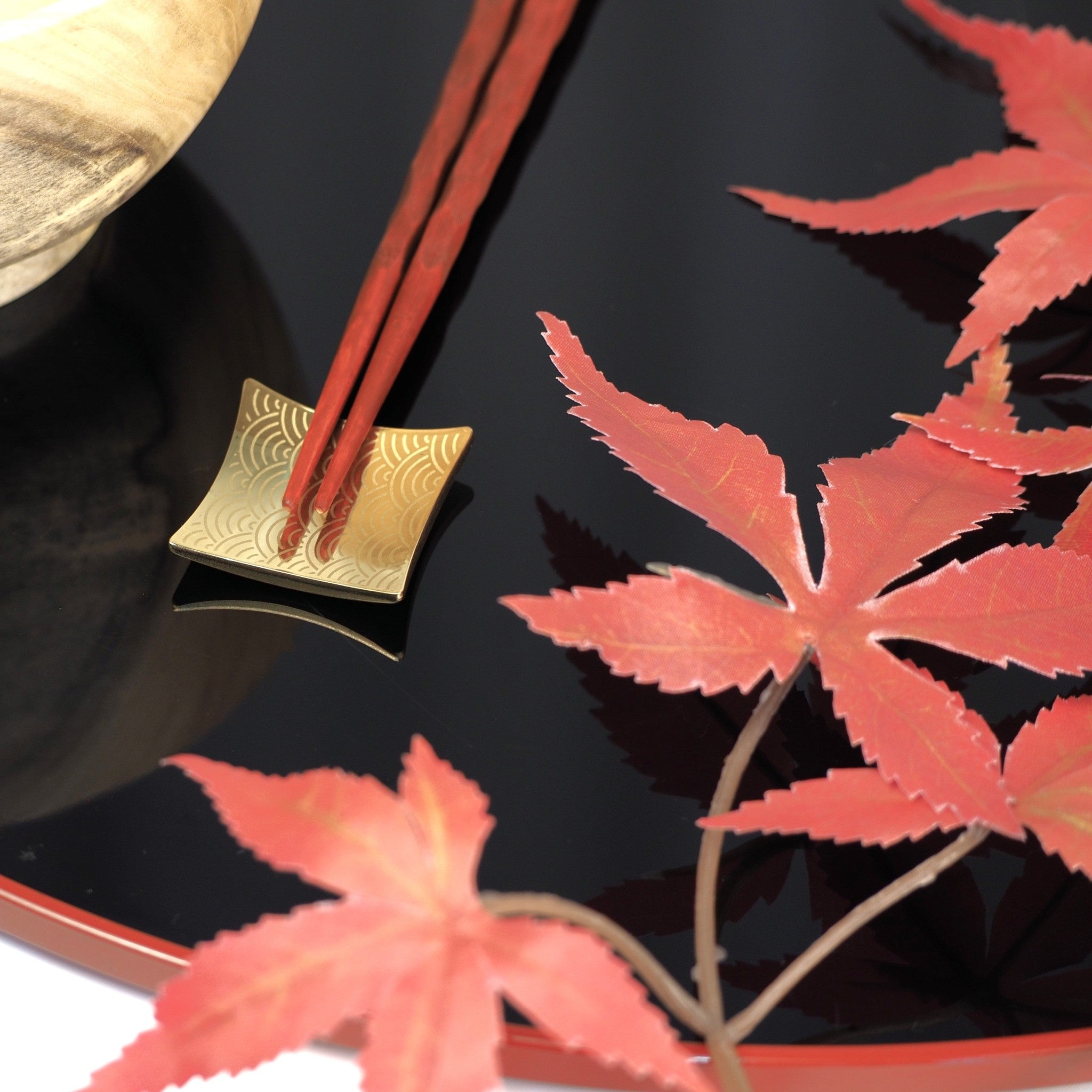 Chopsticks resting on a Japanese gold chopstick rest against a dark background. Tsukushi