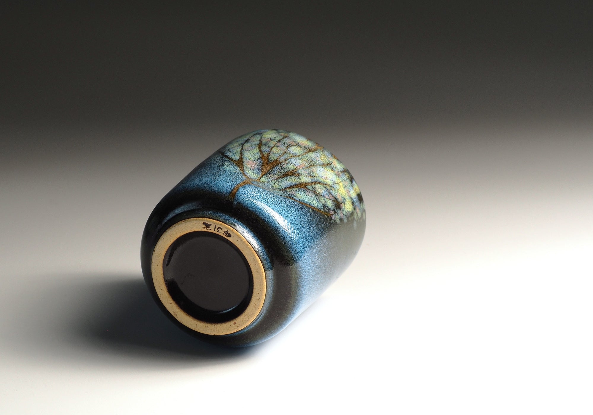 Bottom view of a blue ceramic yunomi with decorative glaze on a gradient background