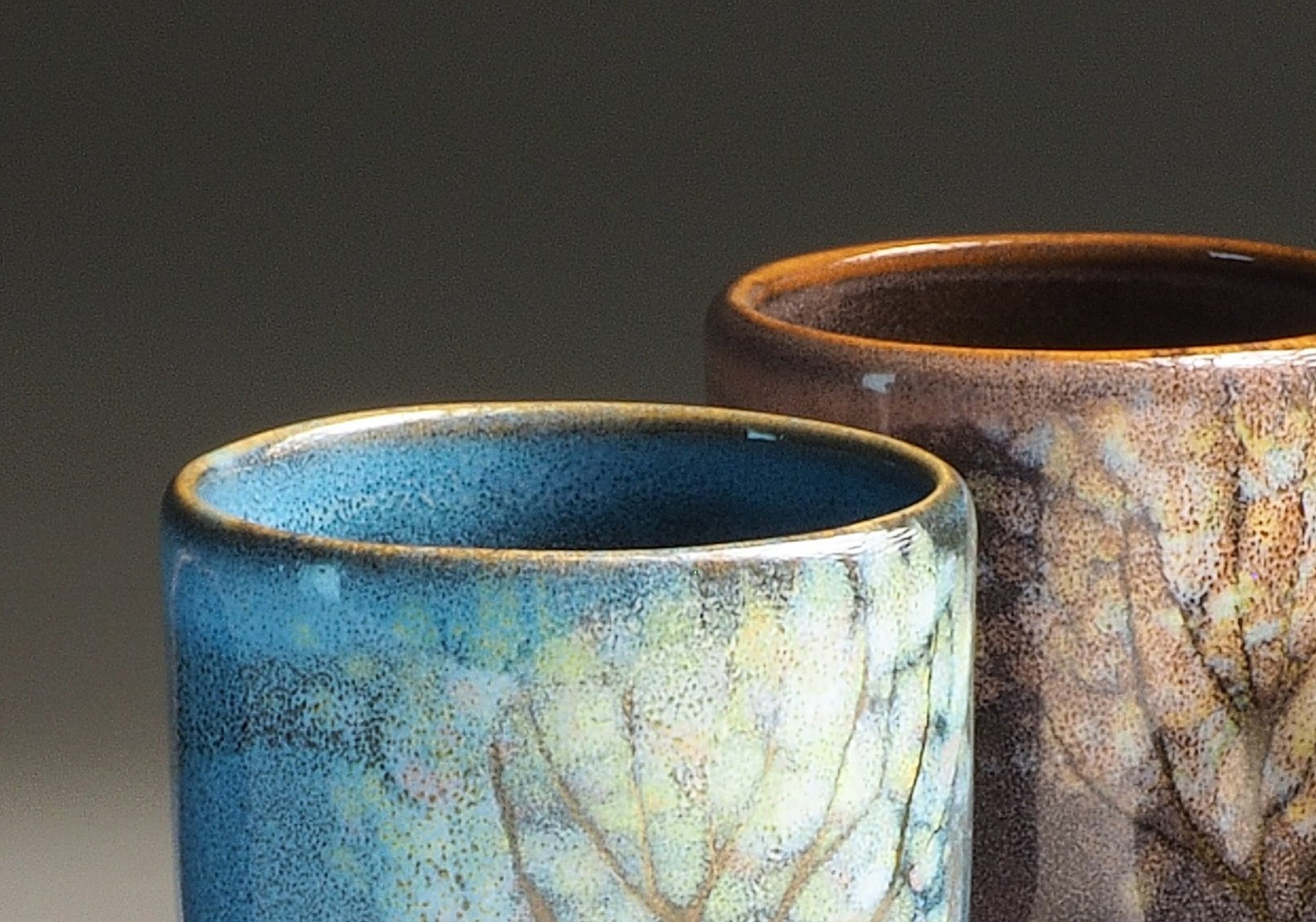 Two Japanese ceramic teacups with tree patterns on a dark background