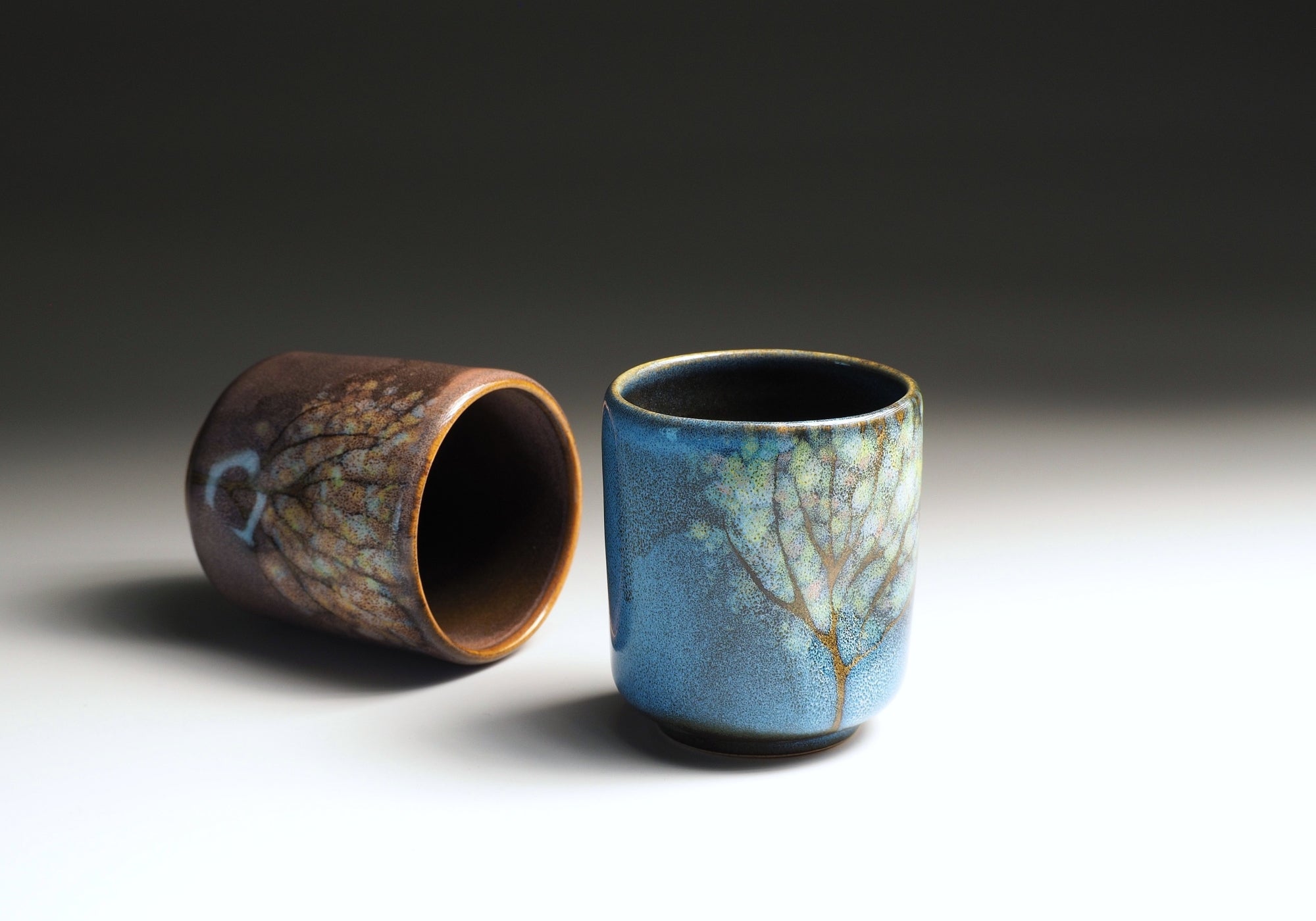 Two pottery yunomi with textured surfaces on a gradient background