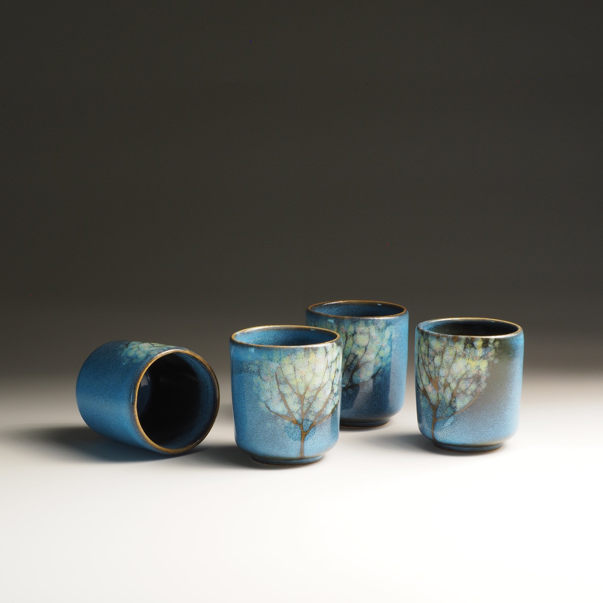 Four blue Japanese ceramic yunomi with tree-like patterns on a gray background