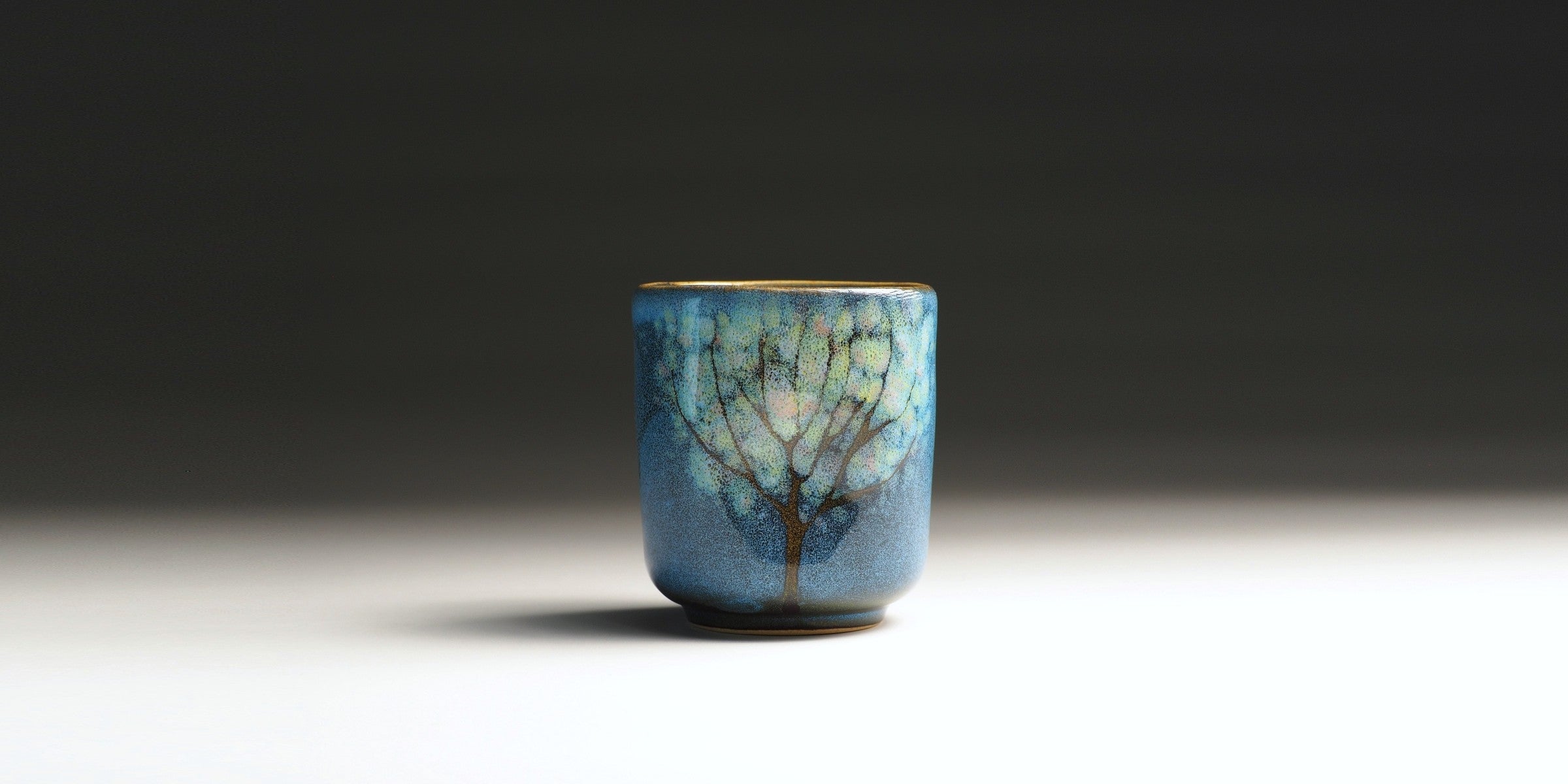 Front view of a blue Japanese yunomi teacup with tree motifs.