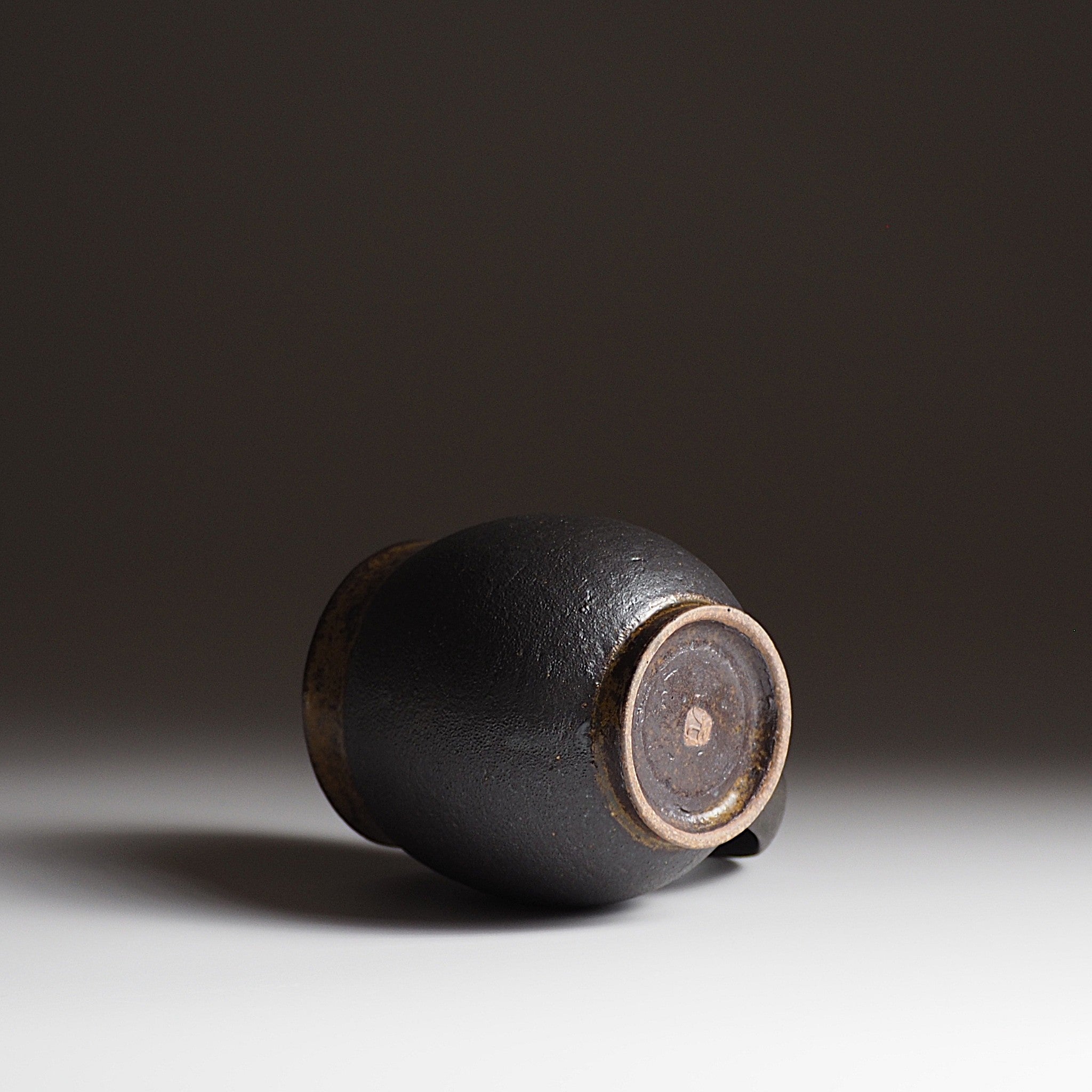 Bottom view of  handcrafted black Japanese ceramic tea mug on a white surface with a dark background, Tsukush