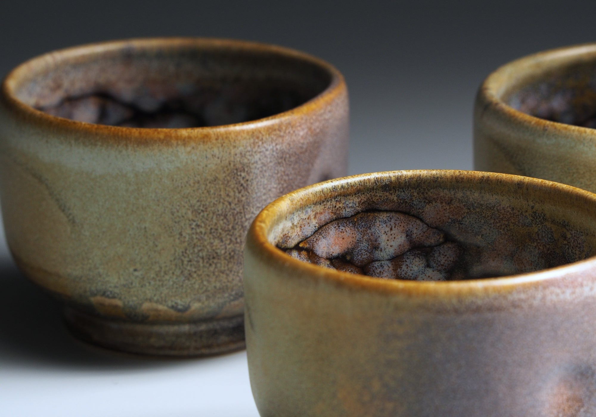 Close-up of three Japanese teacups with a sakura-themed glaze on a dark background.