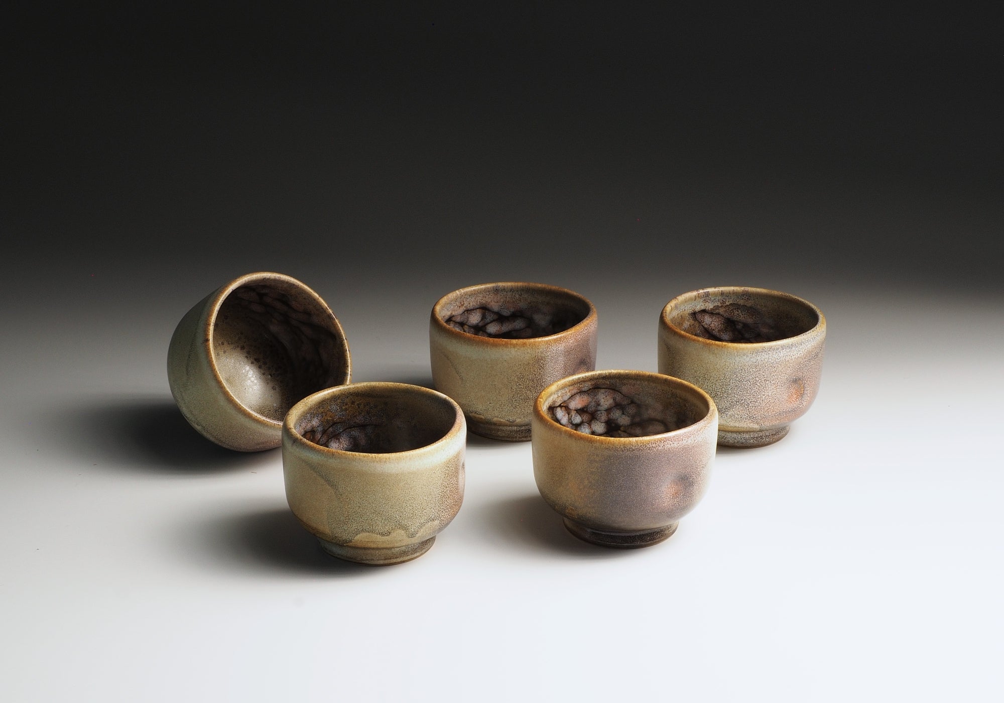 Set of five ceramic Japanese teacups with sakura-themed decorations inside, on a light background.