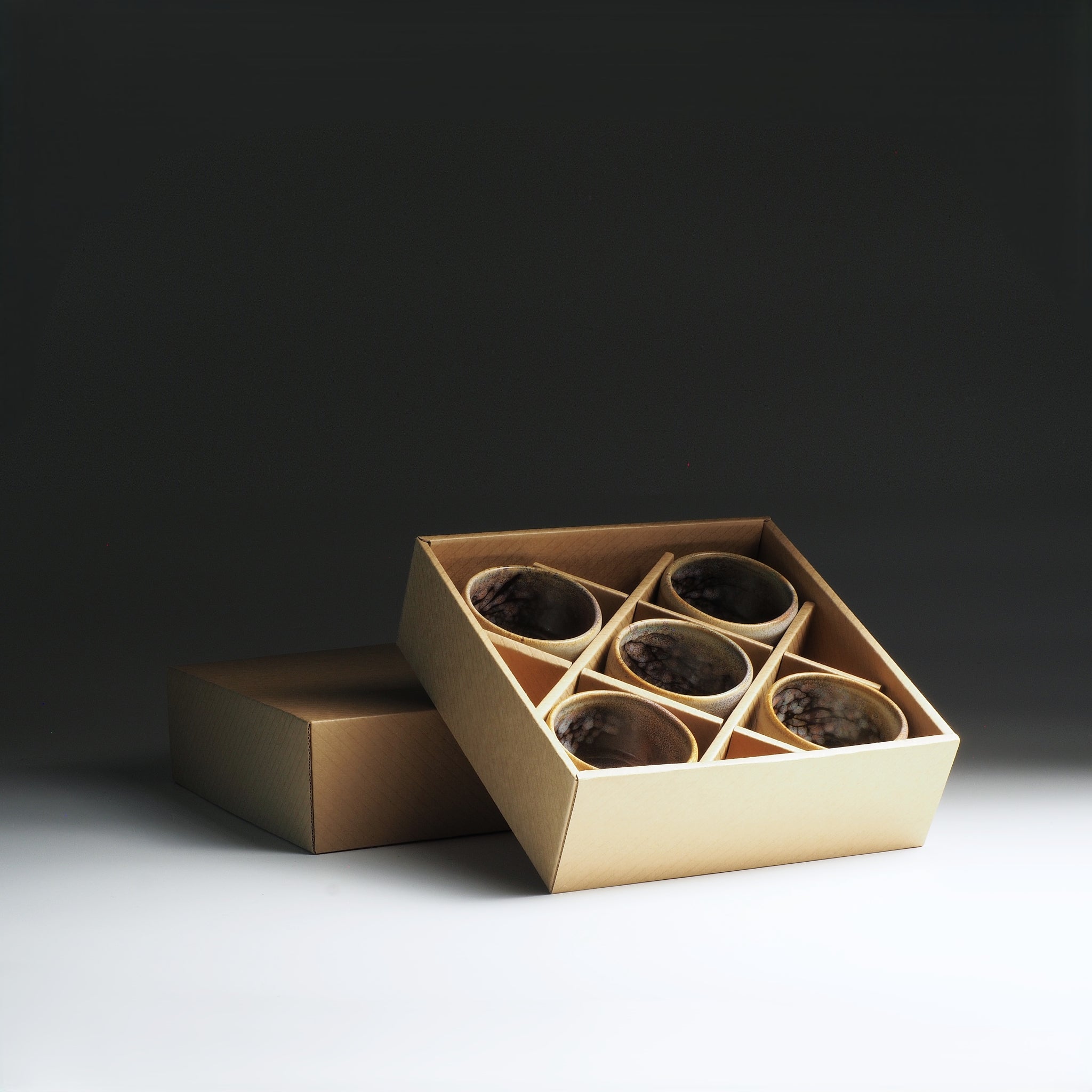 Open cardboard box with inside five Japanese teacups on a dark background
