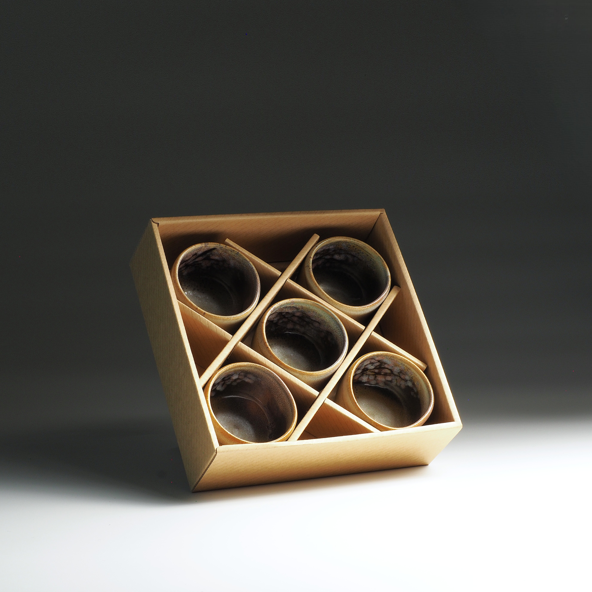 Set of six Japanese yunomi cups in a cardboard box on a dark background