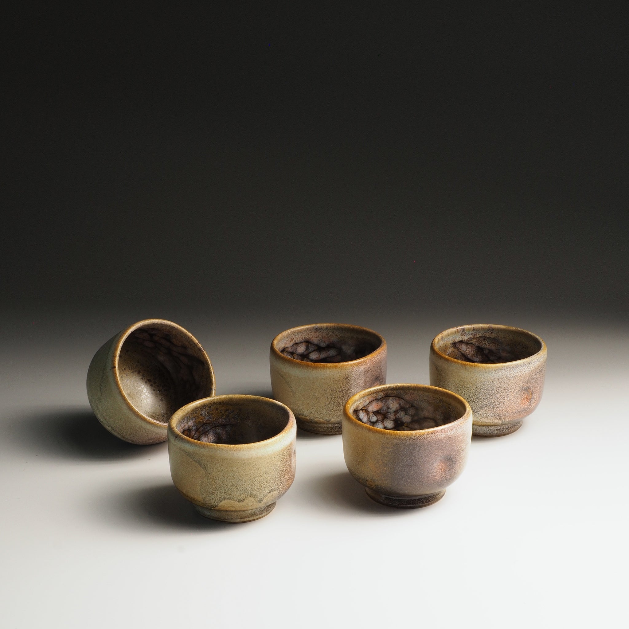 Four pink ceramic yunomi teacups with a textured surface on a gradient background