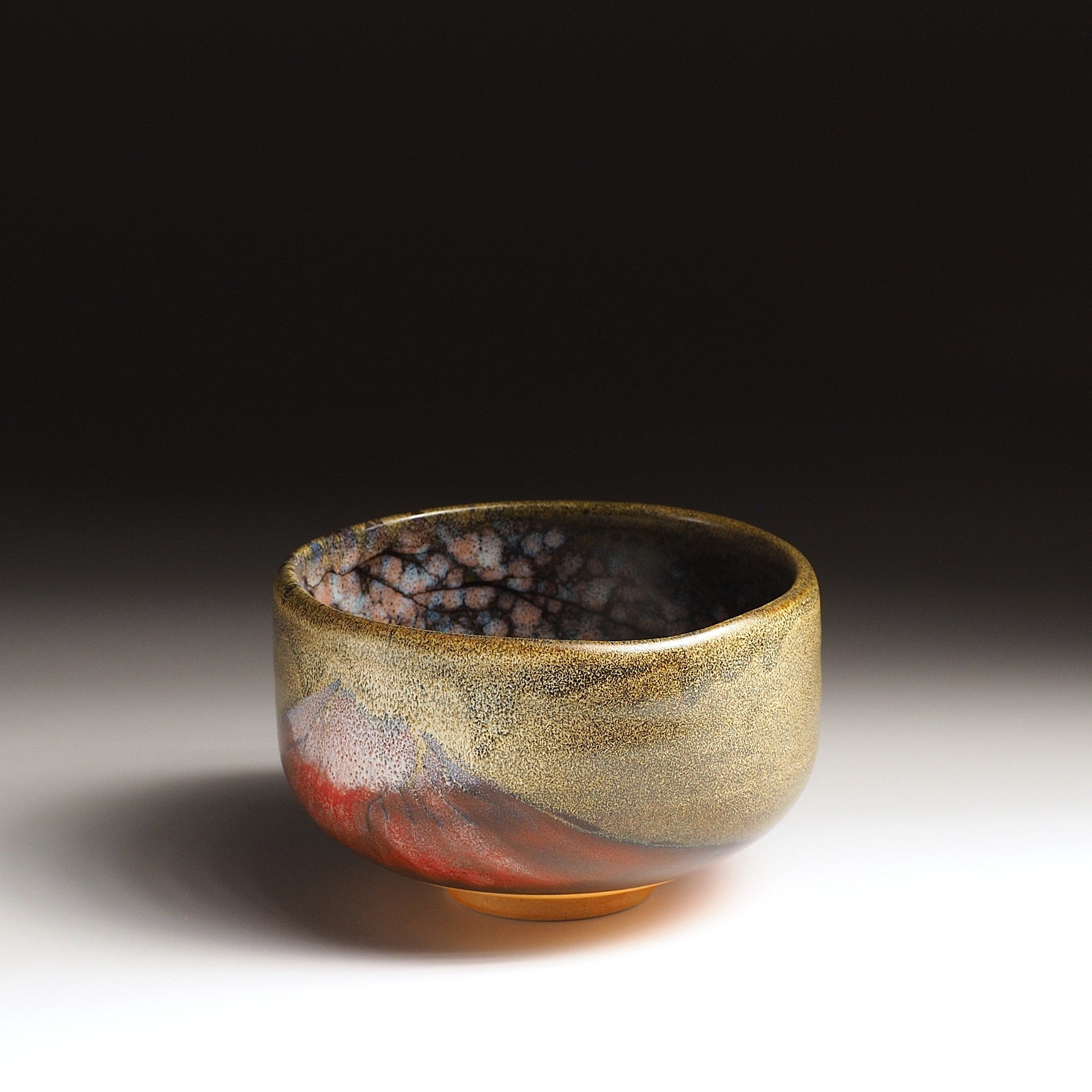 A Japanese ceramic matcha bowl adorned with Red Fuji and cherry blossoms against a black background. Tsukushi.