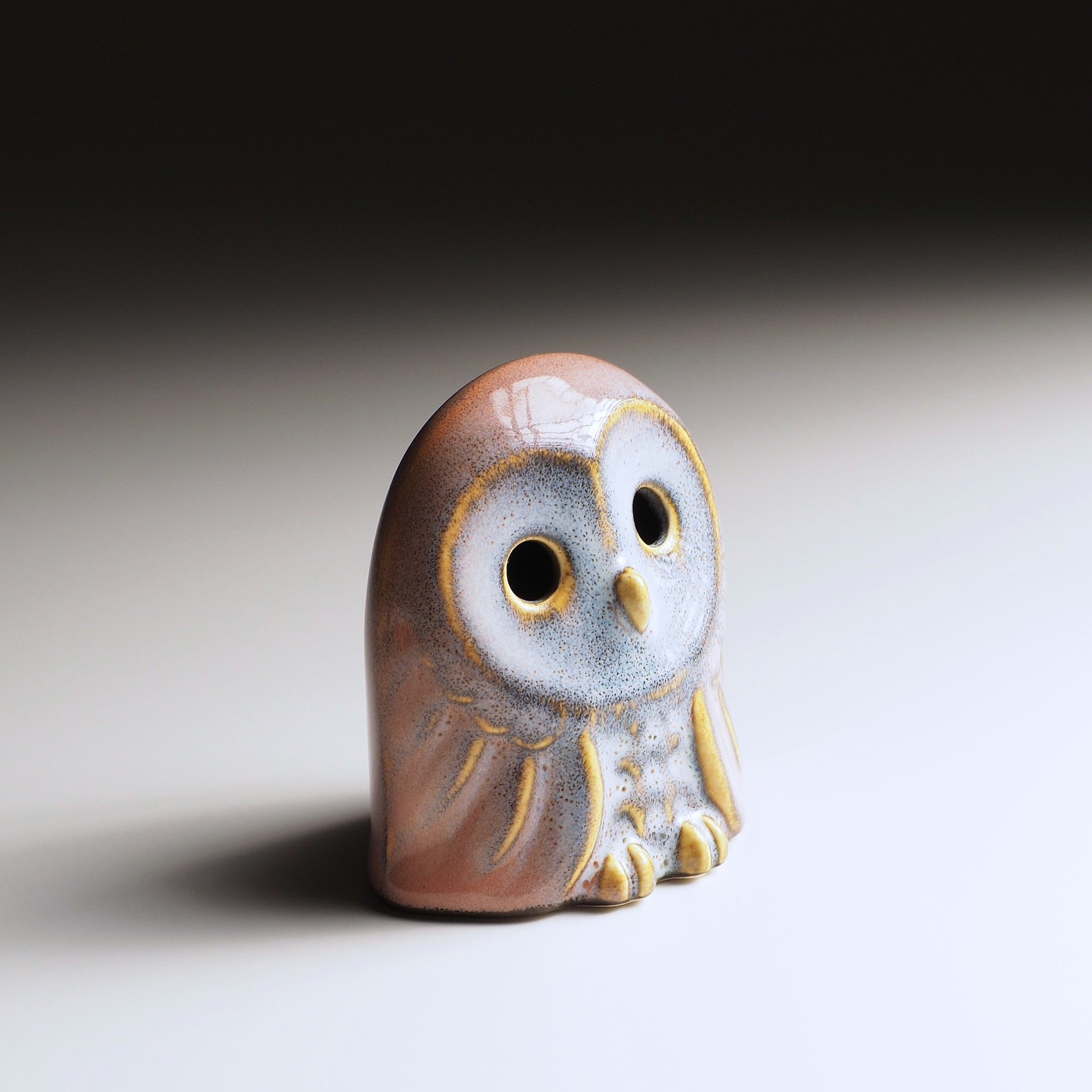Engifuku owl figurine by Kazuhiro Kojima seen from an oblique angle, pink and grey speckled glaze, golden details, hollow eyes.