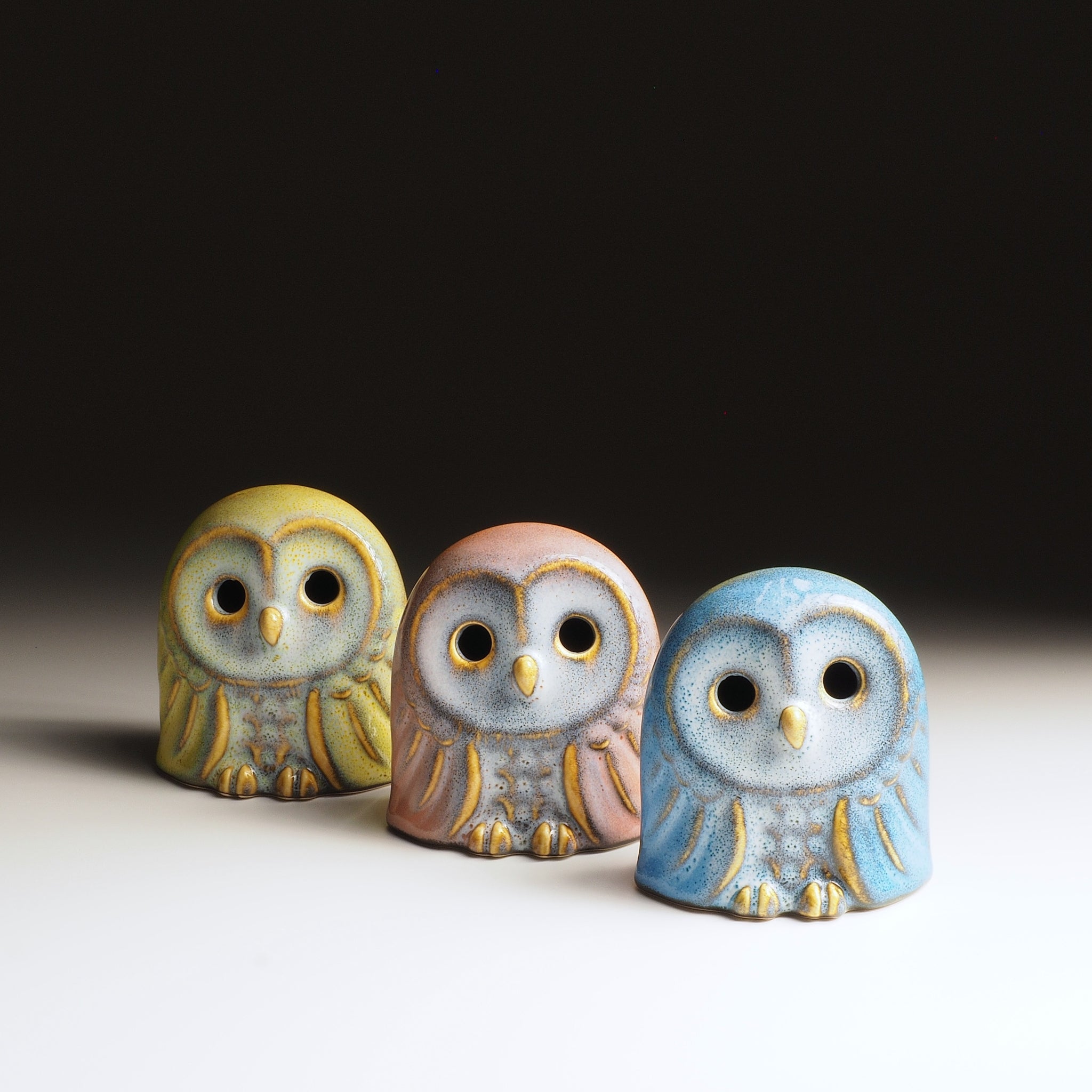 Set of three Engifuku owl figurines by Kazuhiro Kojima in yellow, pink, and blue speckled glazes, hollow eyes, front view.