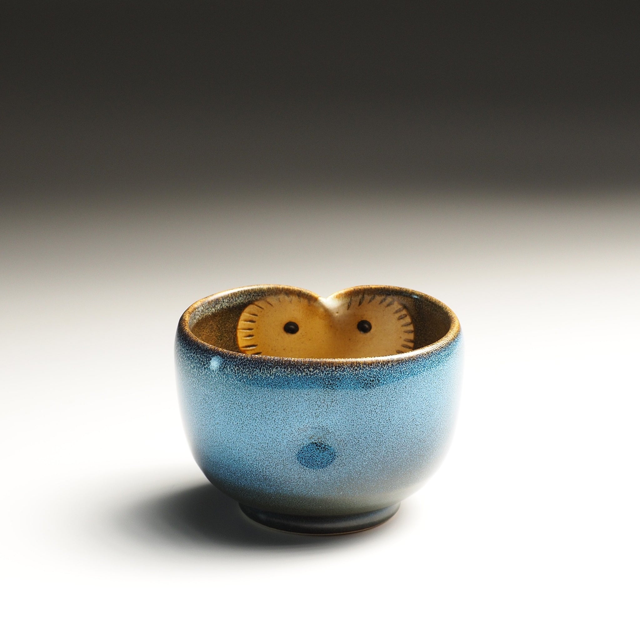 Front view of a Japanese yunomi with owl decoration on the inside, on a gradient background.