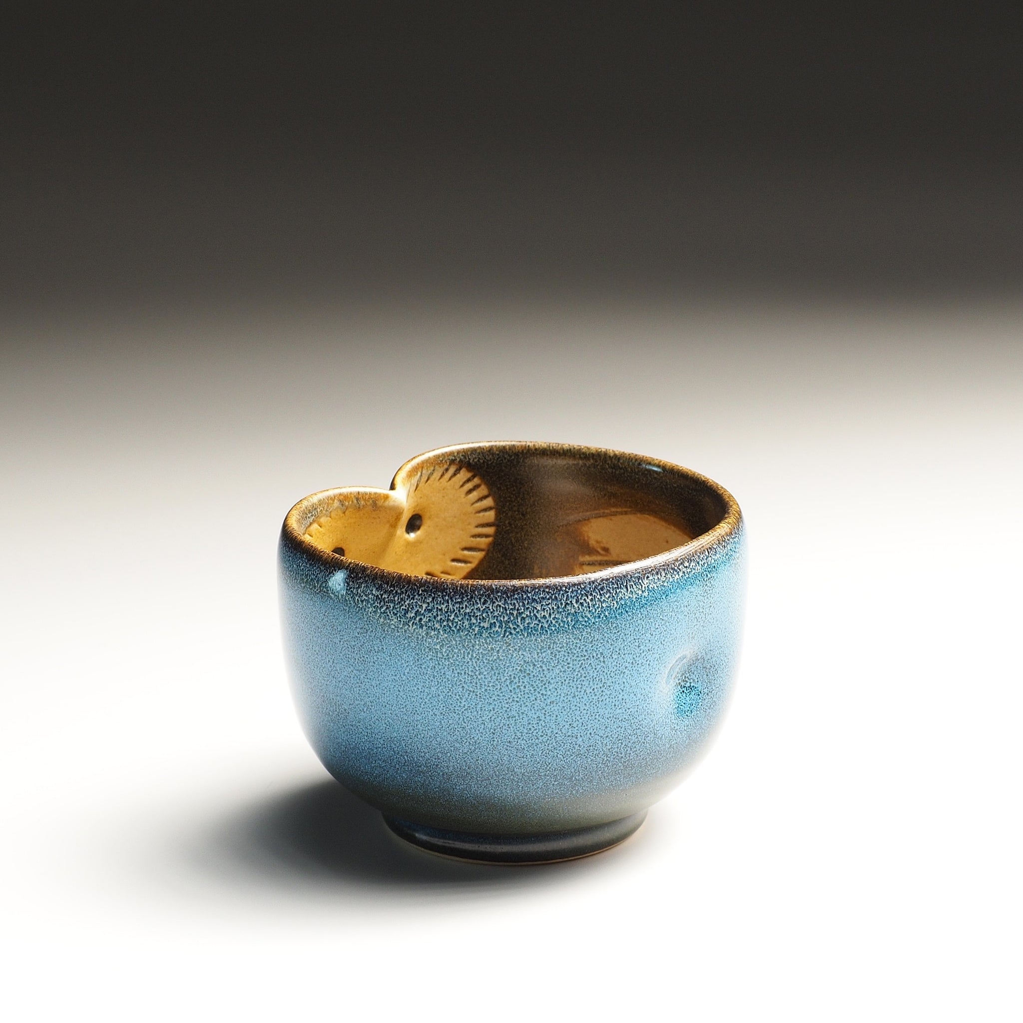 Japanese pottery teacup with owl decorations on the inside, on a gradient background.