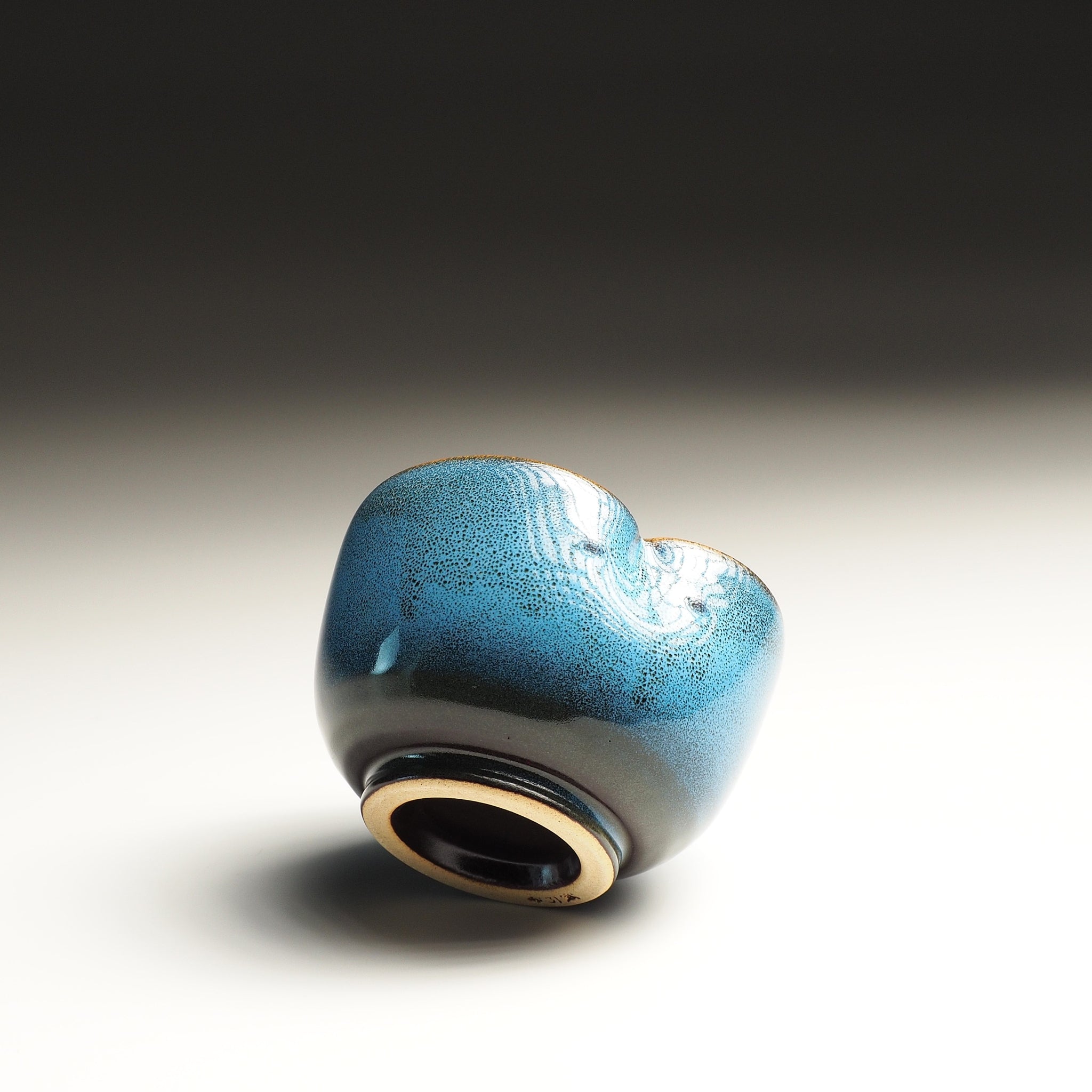 Side-bottom view of a Japanese yunomi with owl decoration on the inside, on a gradient background.