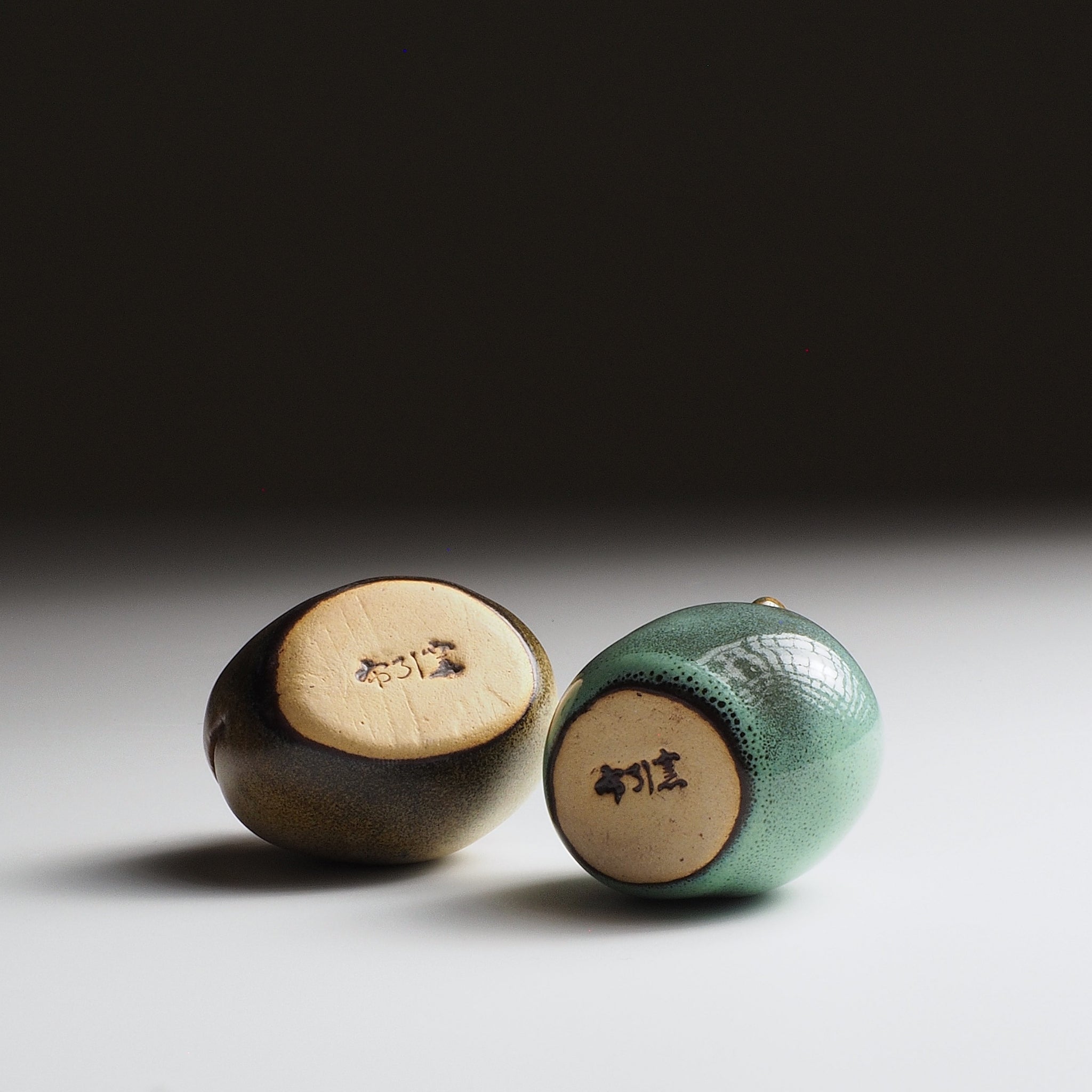 Bottom view of two Gofuku ceramic owl figurines showing artist signatures carved into cream-colored base surfaces.