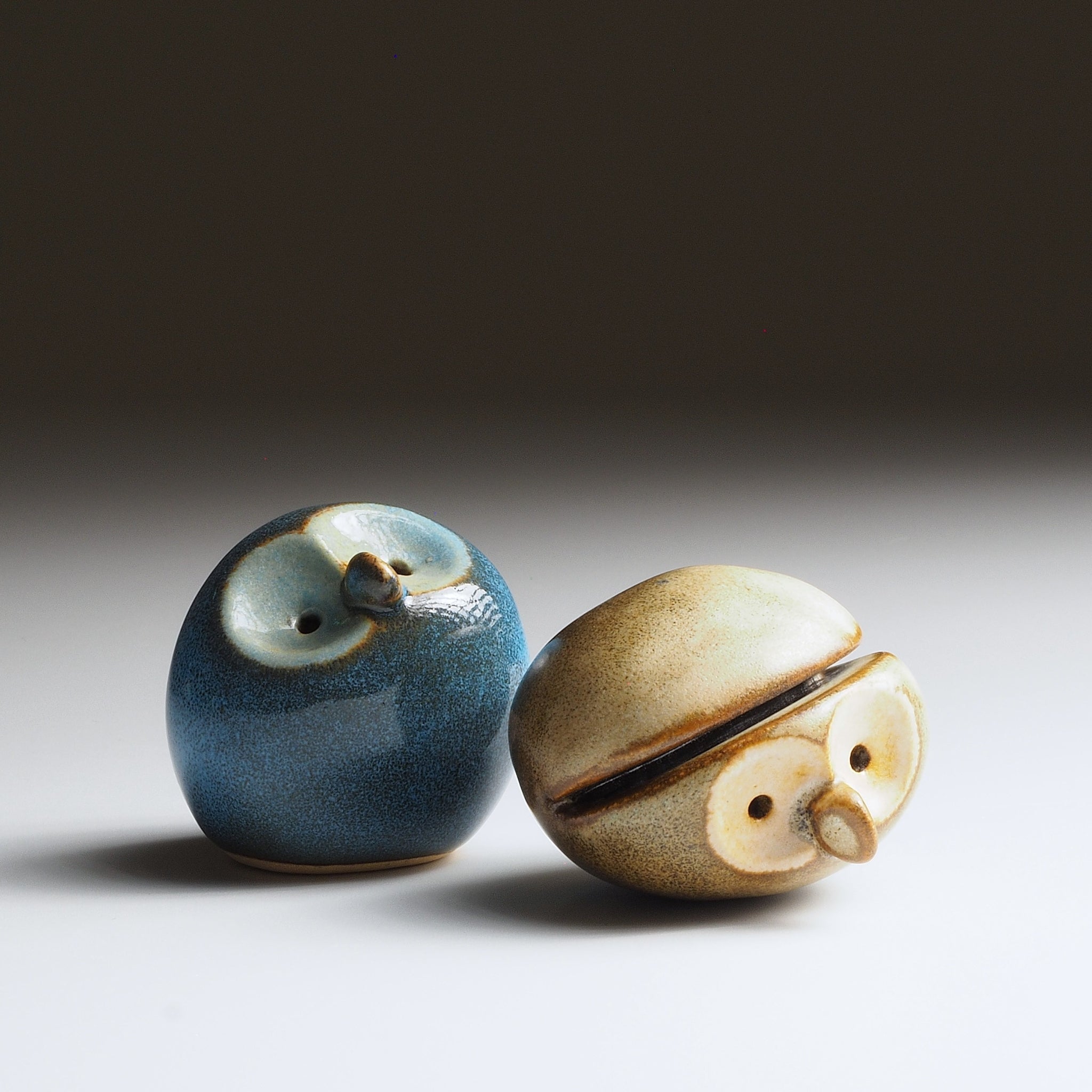 Pair of Gofuku ceramic owl figurines in twilight blue and warm sandstone, showcasing handcrafted form and Nanasai Tenmoku glaze.