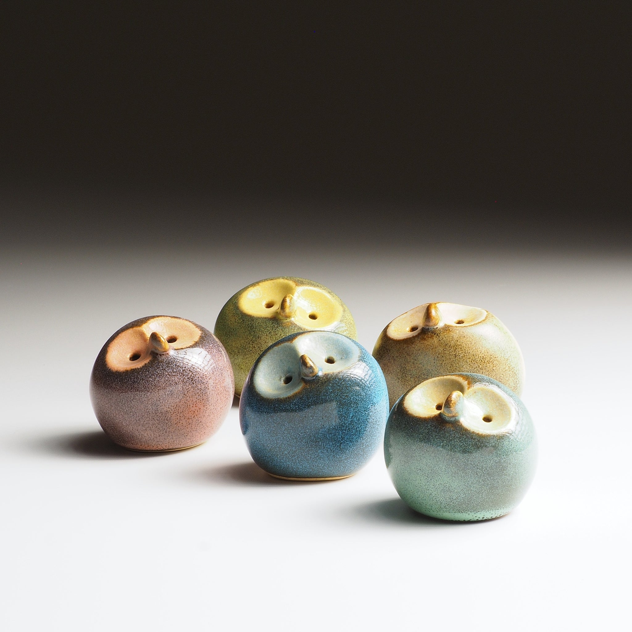 Five handcrafted ceramic owl figurines in teal, plum, sandstone, twilight blue, and moss green with gold-glazed faces.