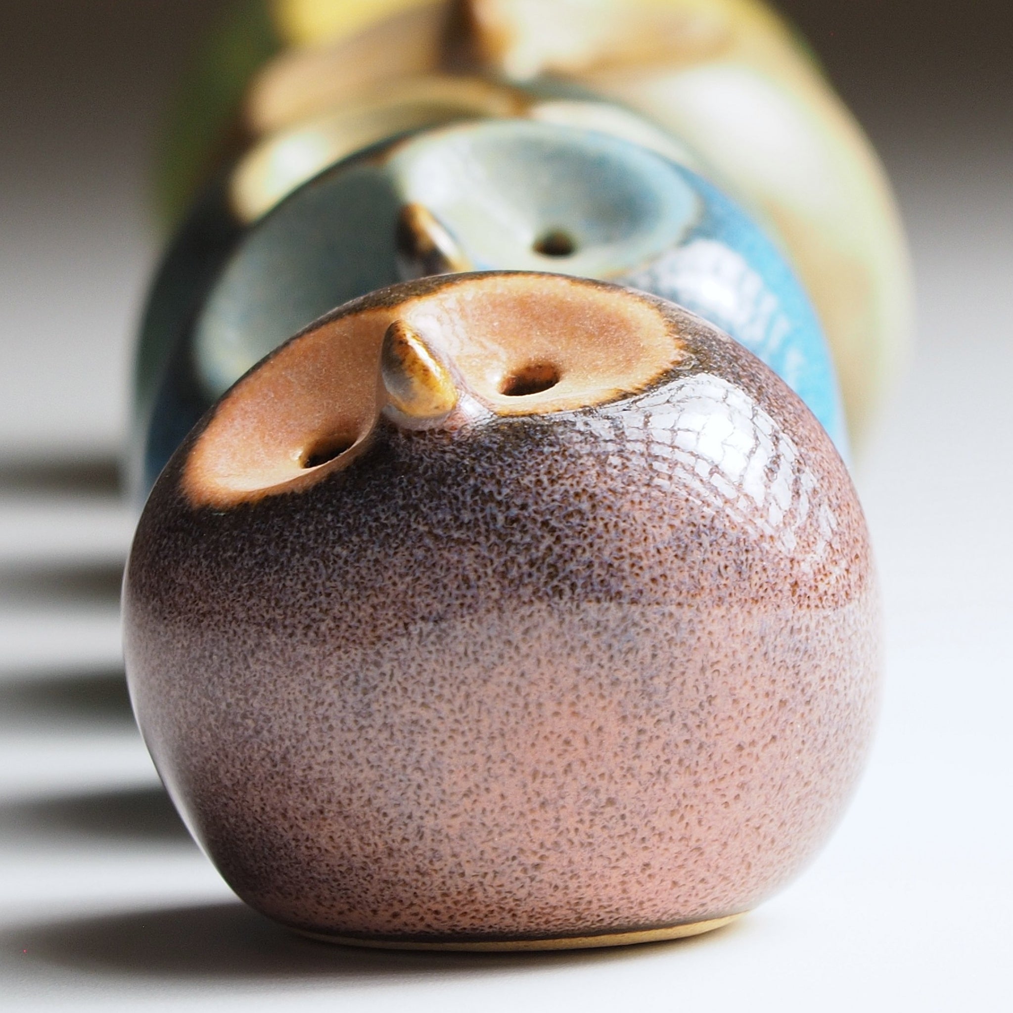 Close-up detail of dusk plum Gofuku ceramic owl figurine showing textured glaze surface and gold beak with others blurred behind.