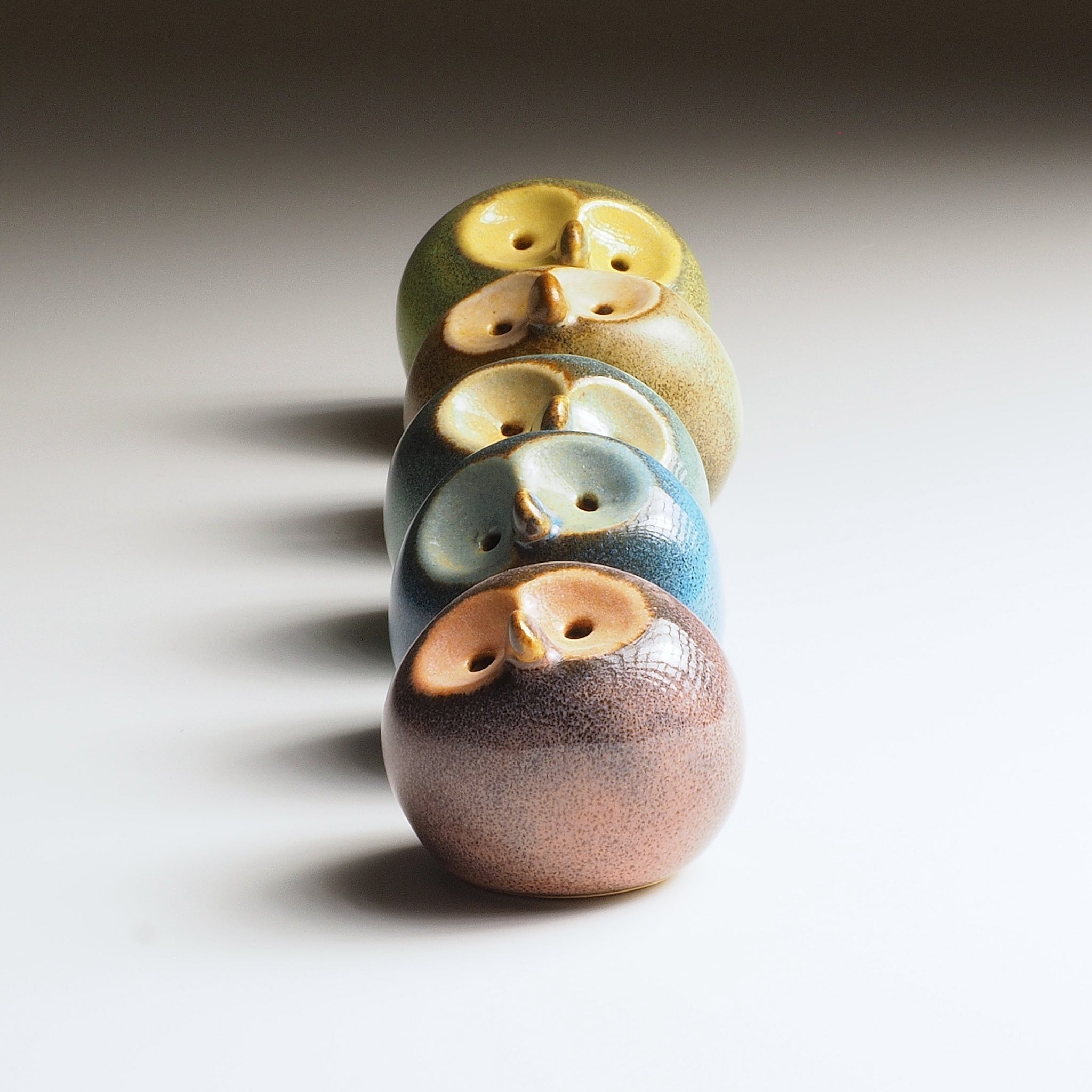 Row of ceramic owl figurines with gradient colors on a neutral background